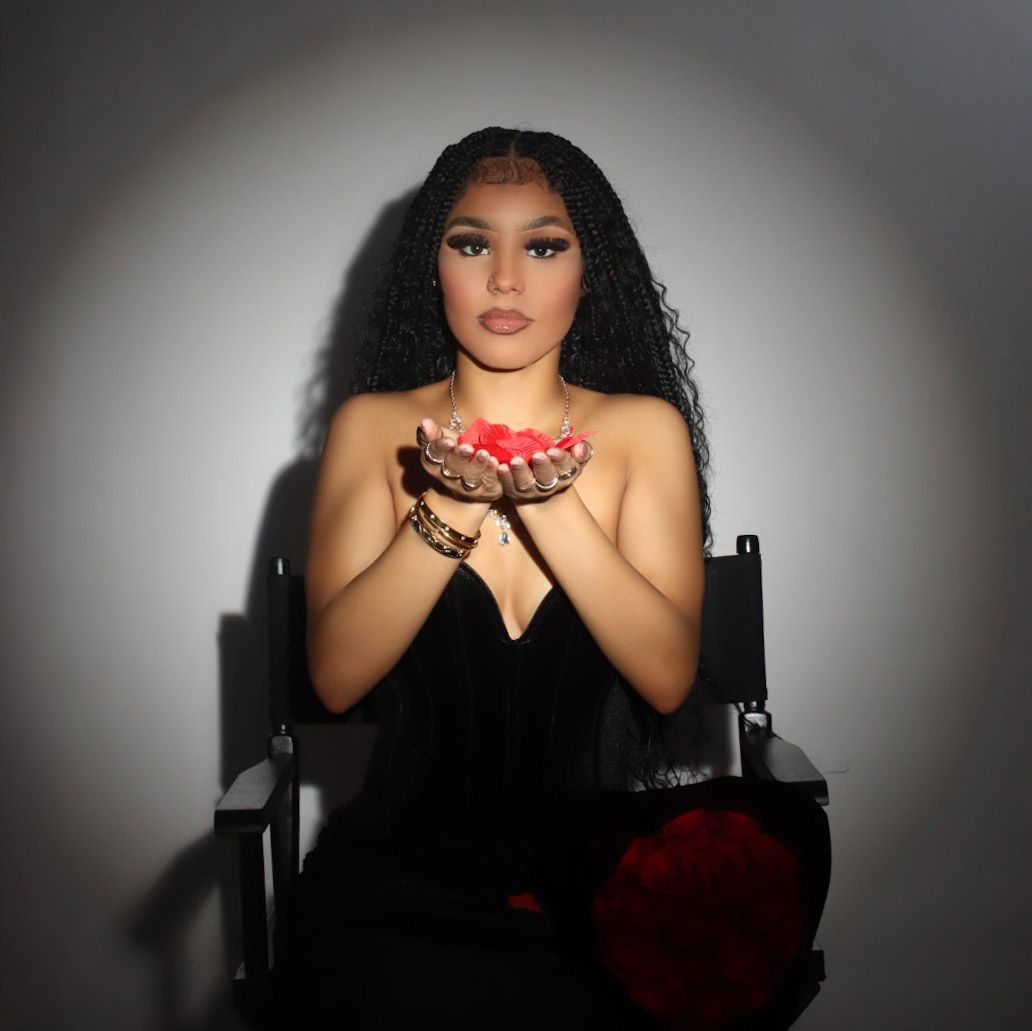 Woman in black velvet dress holding red rose petals in cupped hands in dramatic studio portrait.