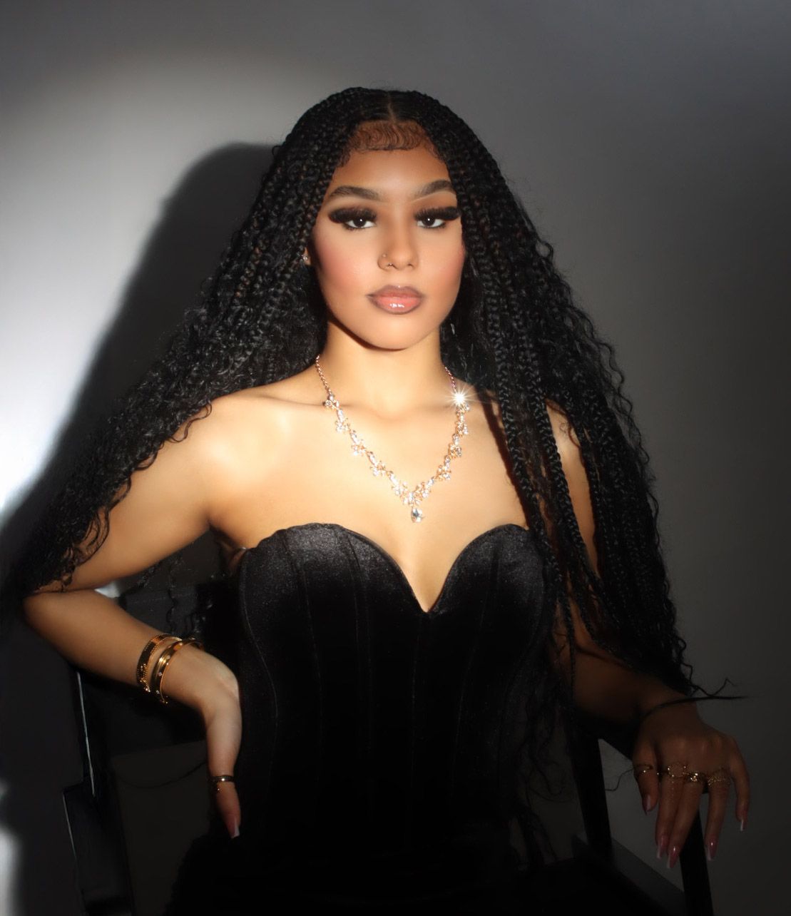 Woman with long braided hair wearing black strapless corset dress and diamond necklace in studio portrait.