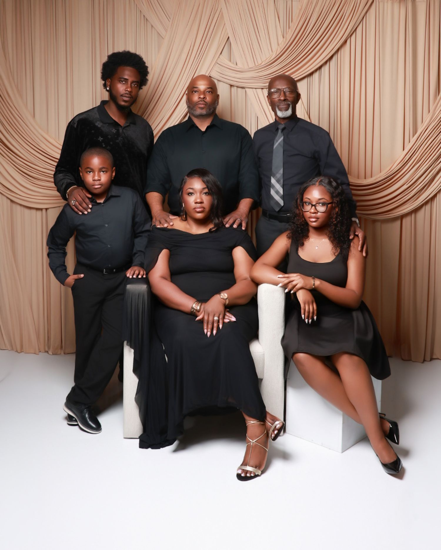 A family of six in coordinated black outfits poses for a formal studio portrait with draped backdrop.