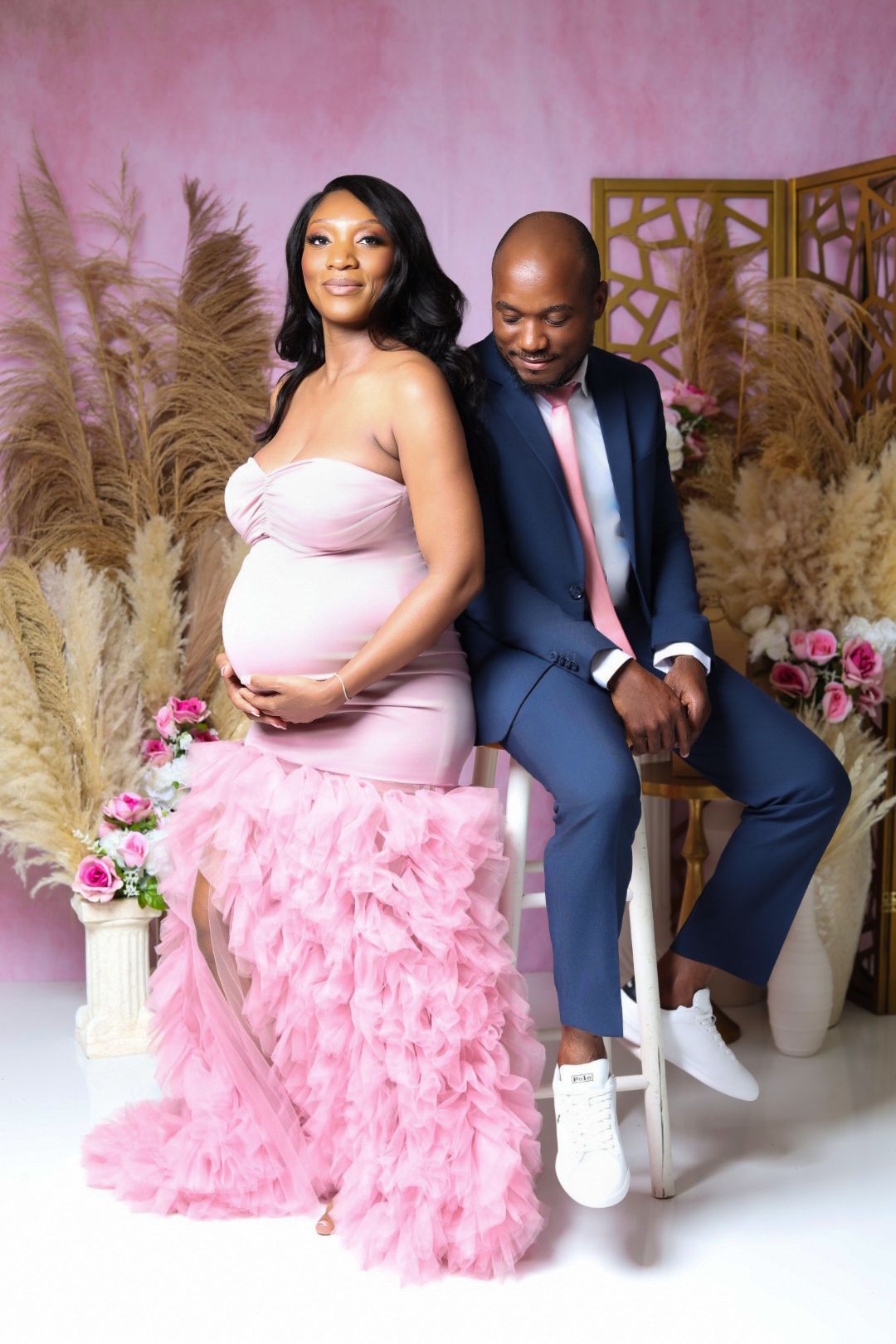 Couple maternity portrait with pregnant woman in pink strapless gown and partner in navy suit sitting together.