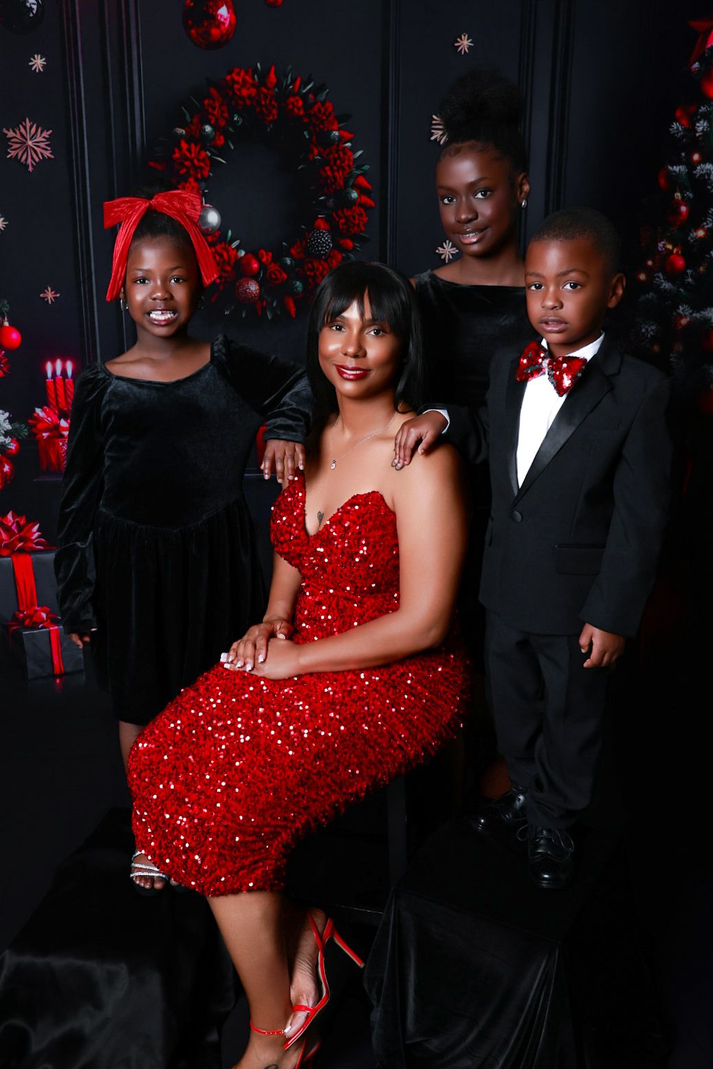 Family of four in red and black holiday outfits posing before Christmas decorations.