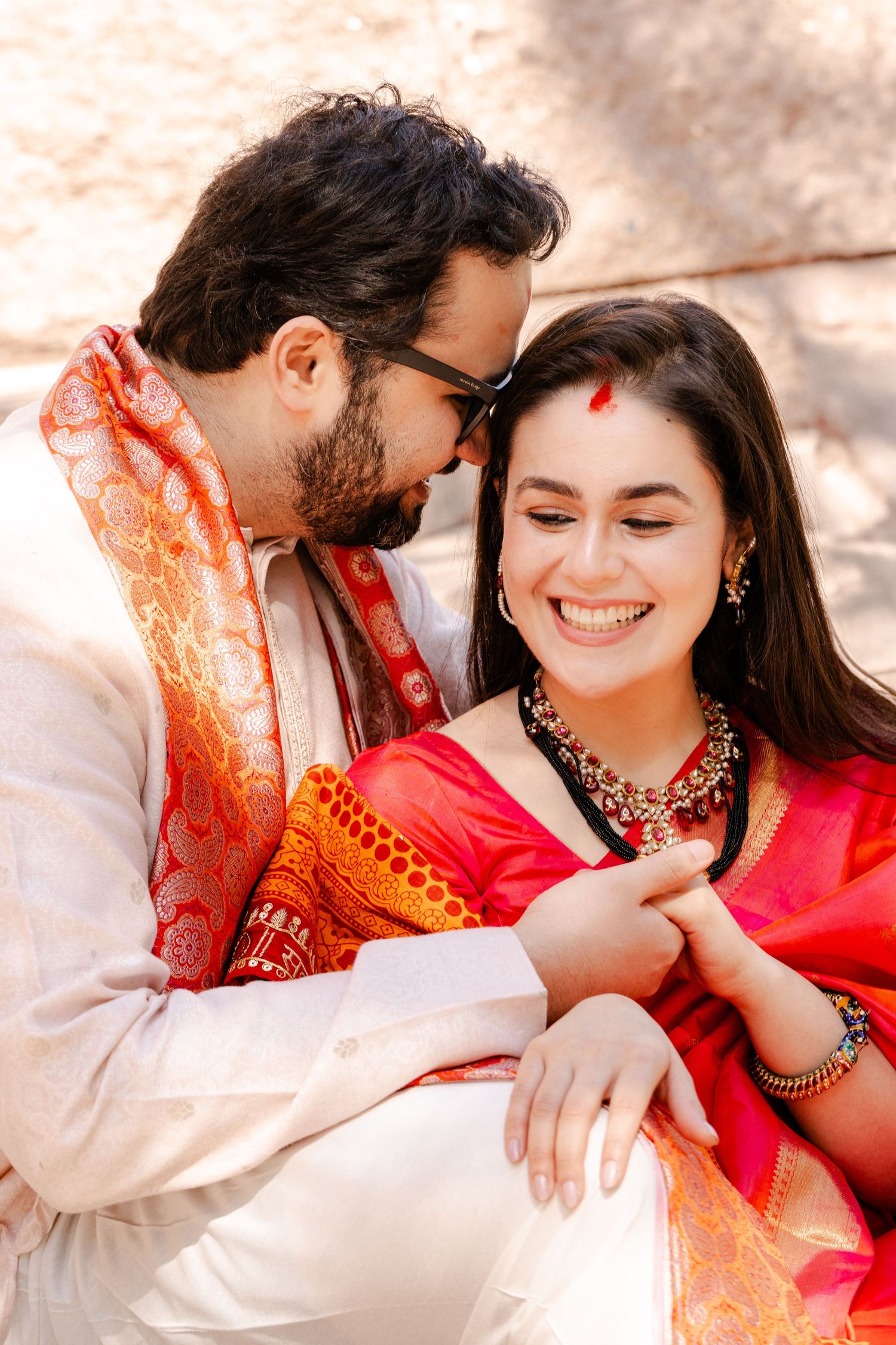 A couple in traditional Indian wedding clothes share an intimate moment outdoors.