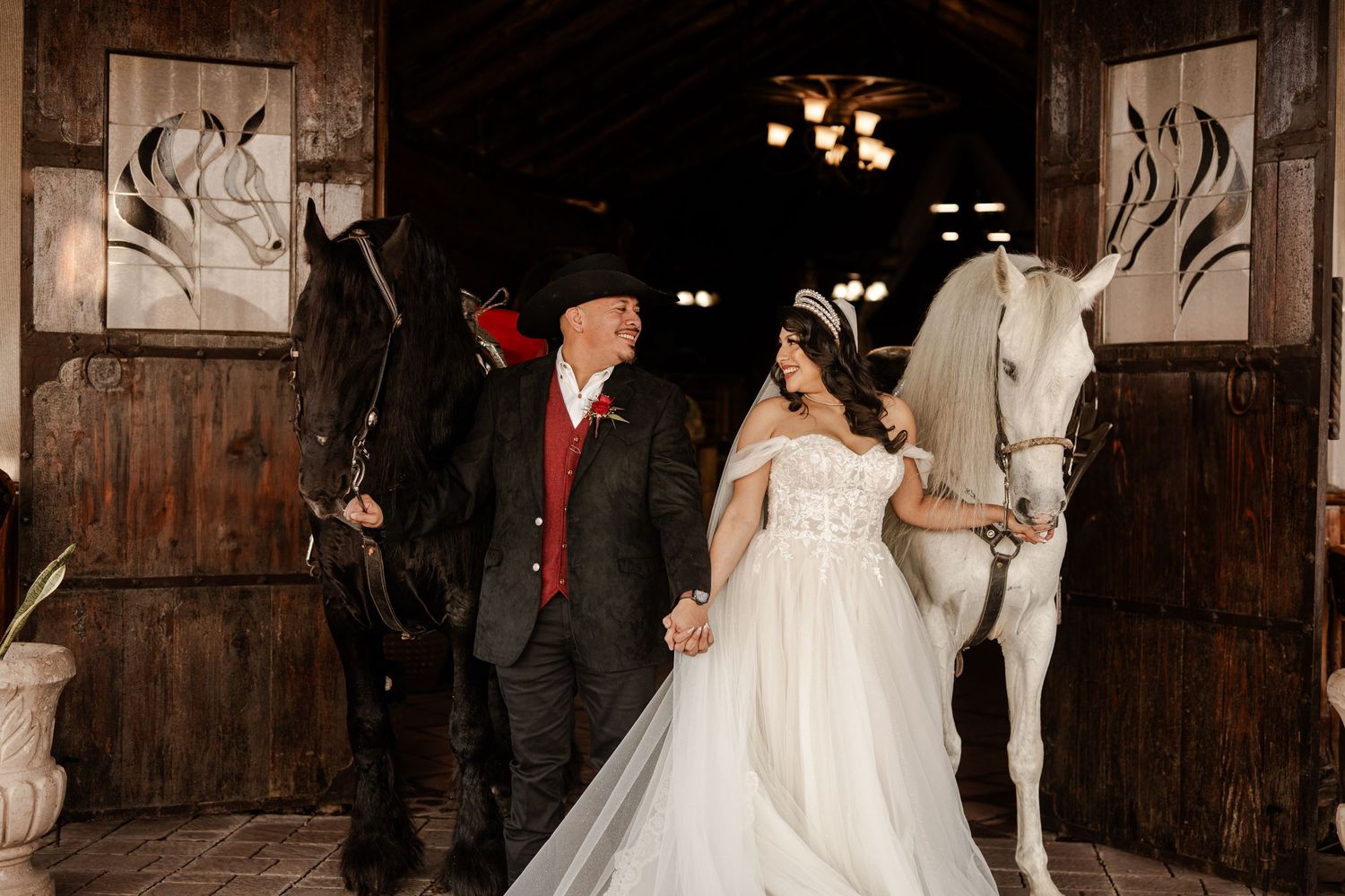 Wedding couple poses with two white horses in rustic barn with wooden panel details.