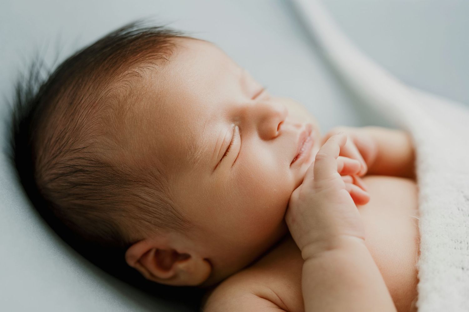 Peaceful sleeping newborn baby in soft natural light resting on white blanket.