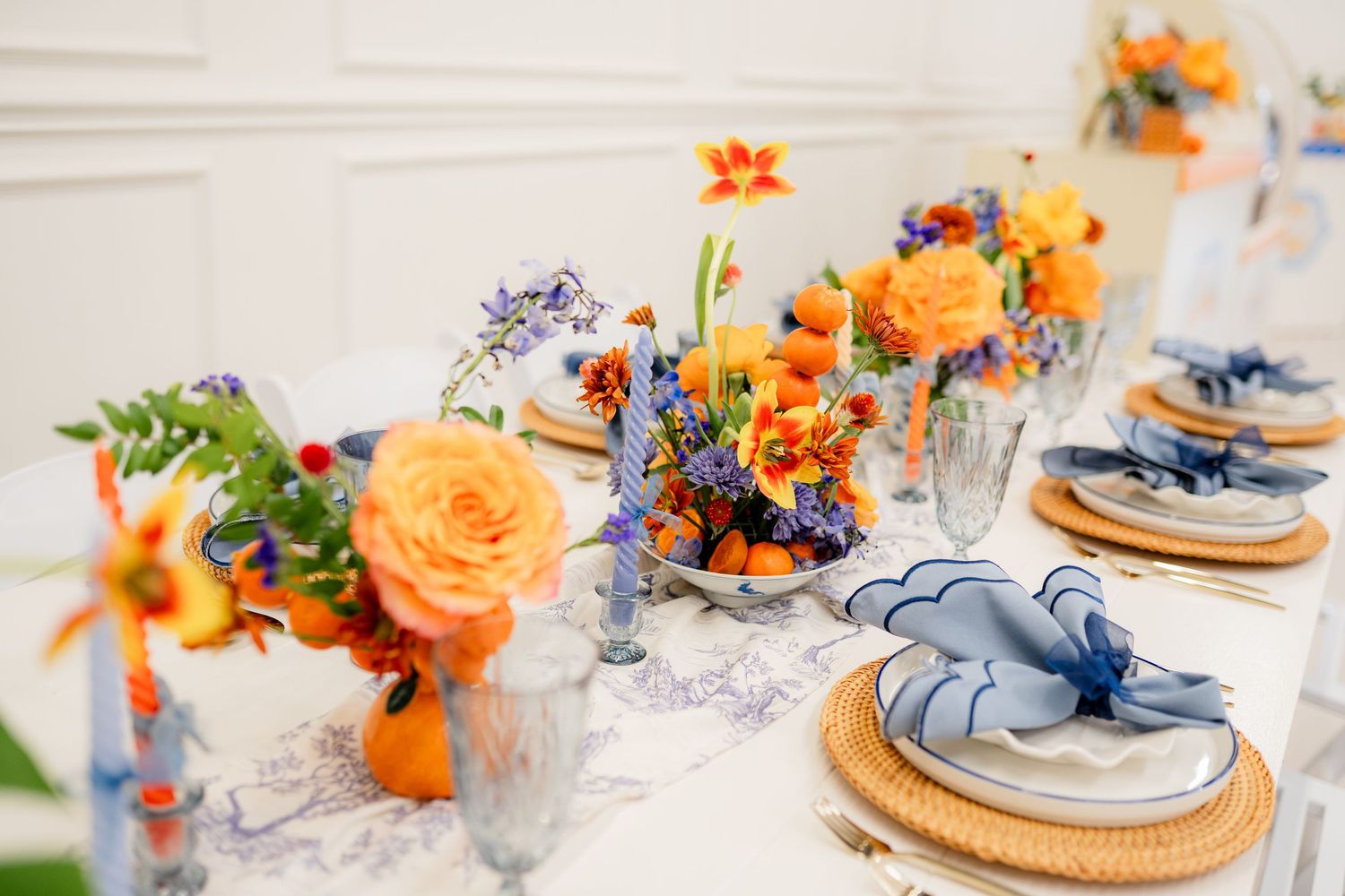 Orange and blue floral wedding table settings with gold chargers and delicate china create an elegant reception design.