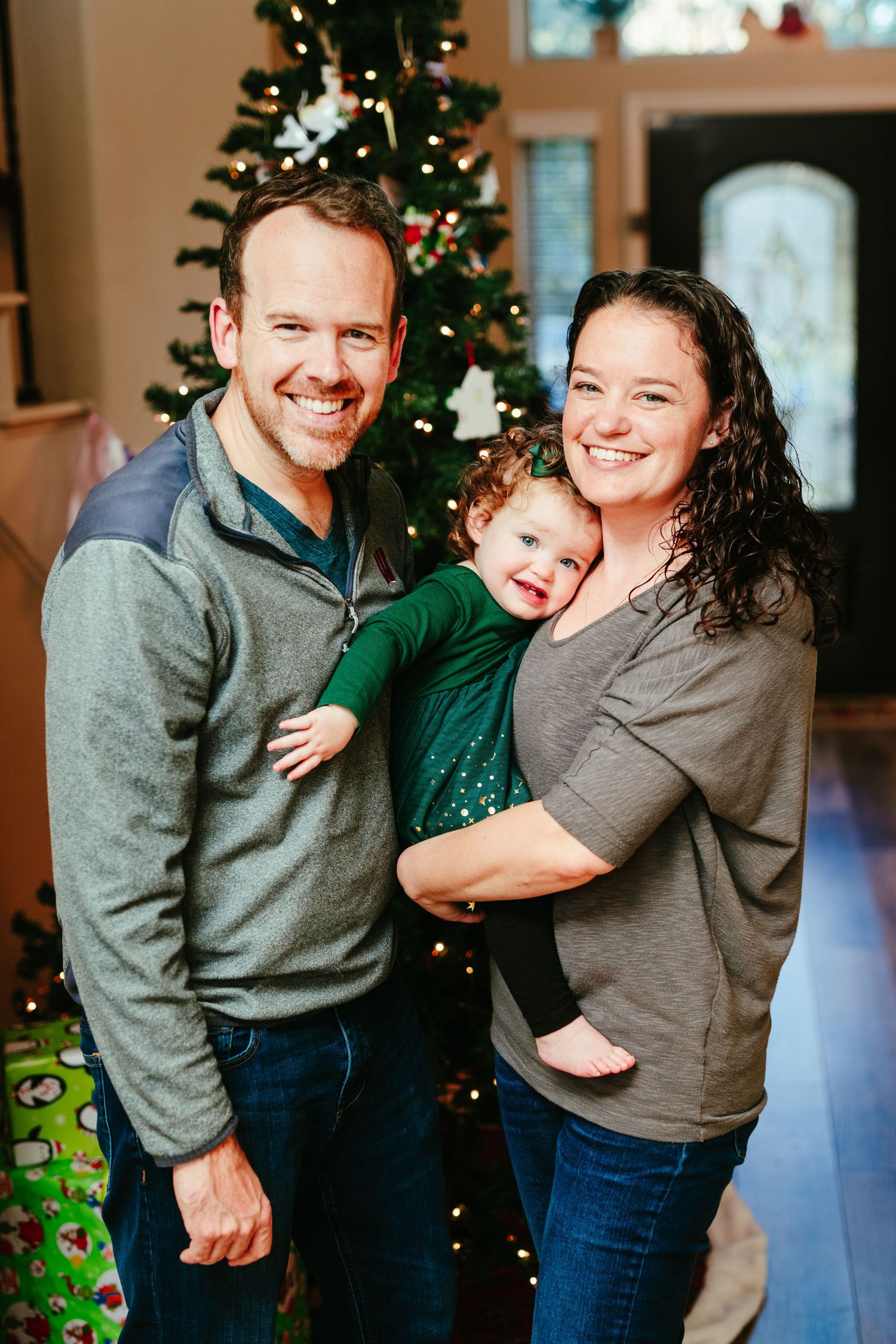 A cheerful family moment captured in front of a decorated Christmas tree with wrapped gifts.