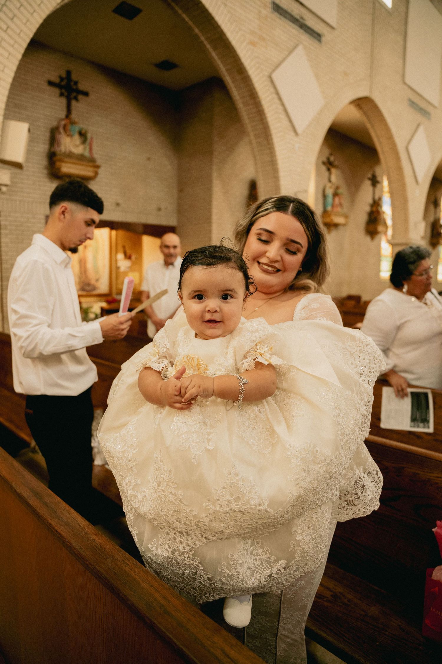 A joyful christening ceremony in a church with a baby wearing an ornate white lace dress.