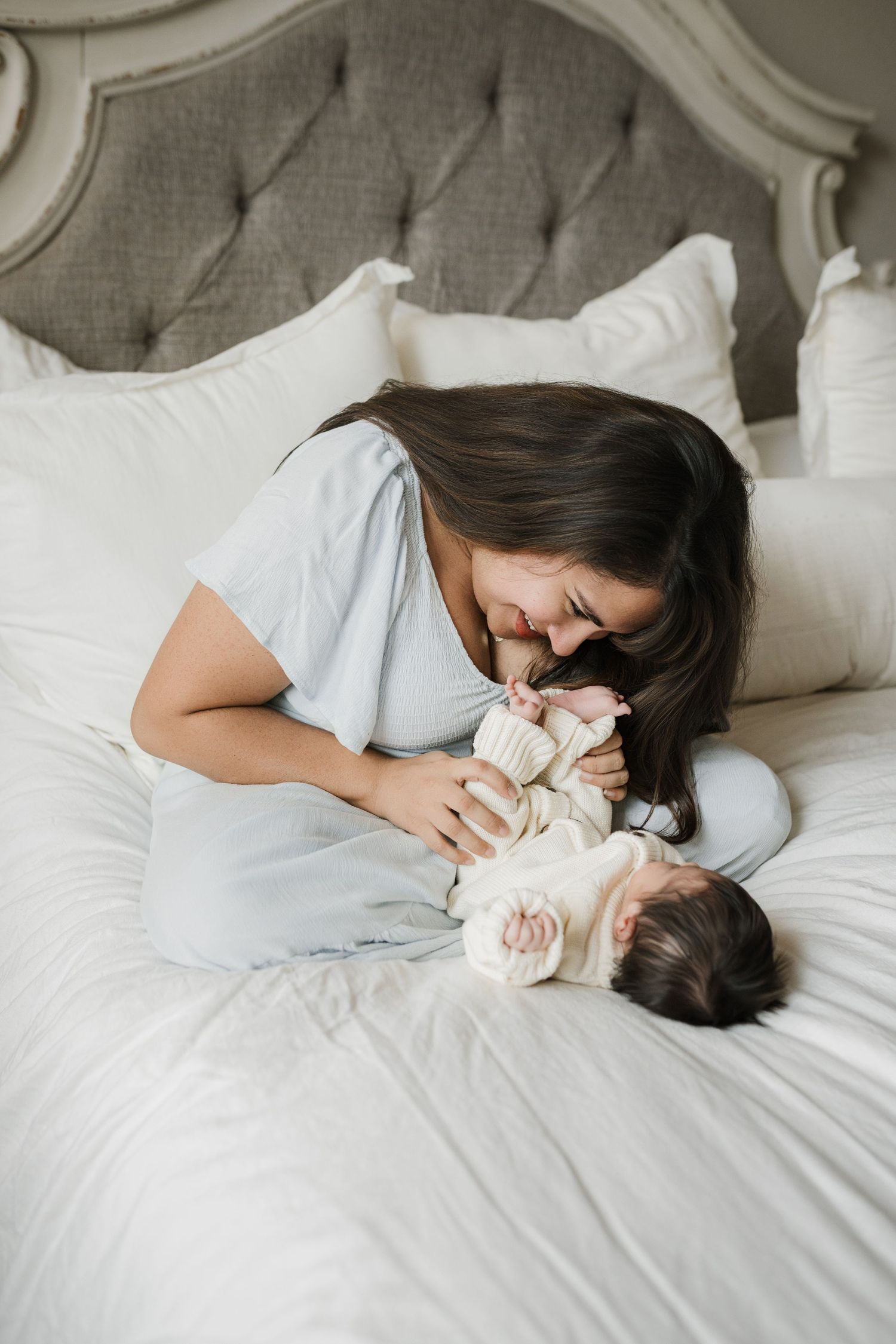 A tender moment captured in soft light as a mother and baby lie together on white bedding.
