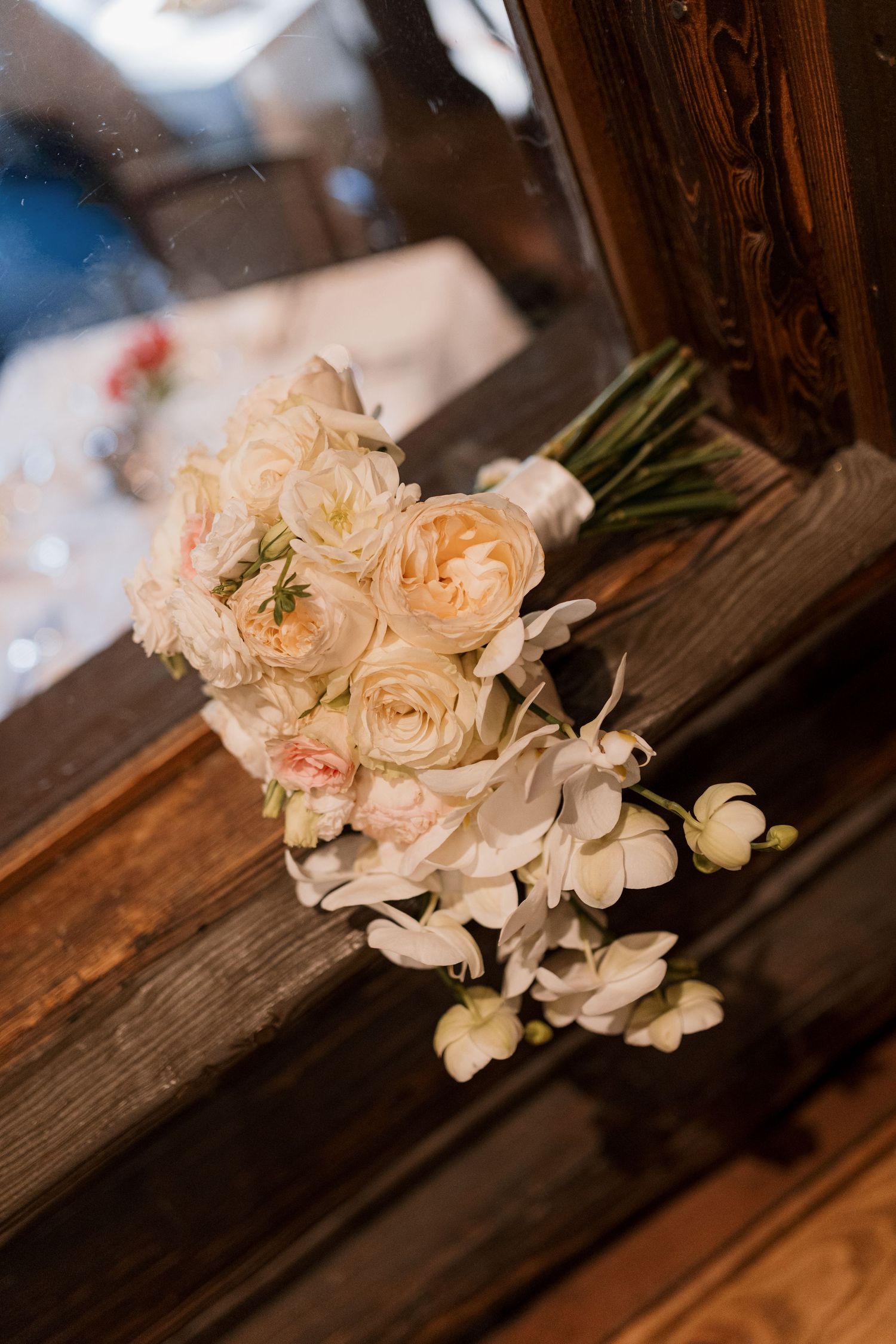 Elegant bridal bouquet of cream roses and white orchids resting on rustic wooden surface.