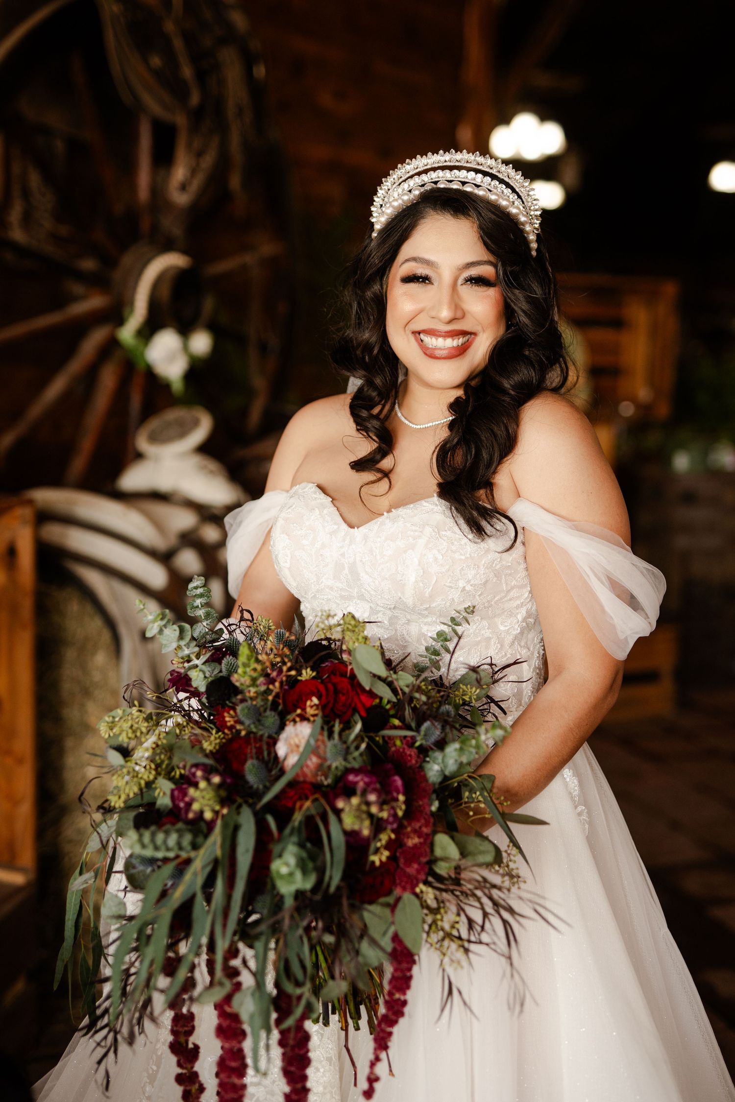 Elegant bridal portrait with dramatic bouquet of burgundy flowers in rustic barn setting.