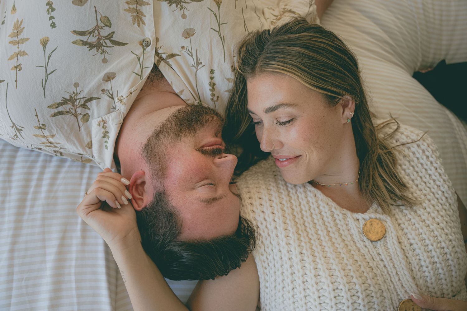 Intimate couple lying together in bed sharing tender moments in soft natural lighting.