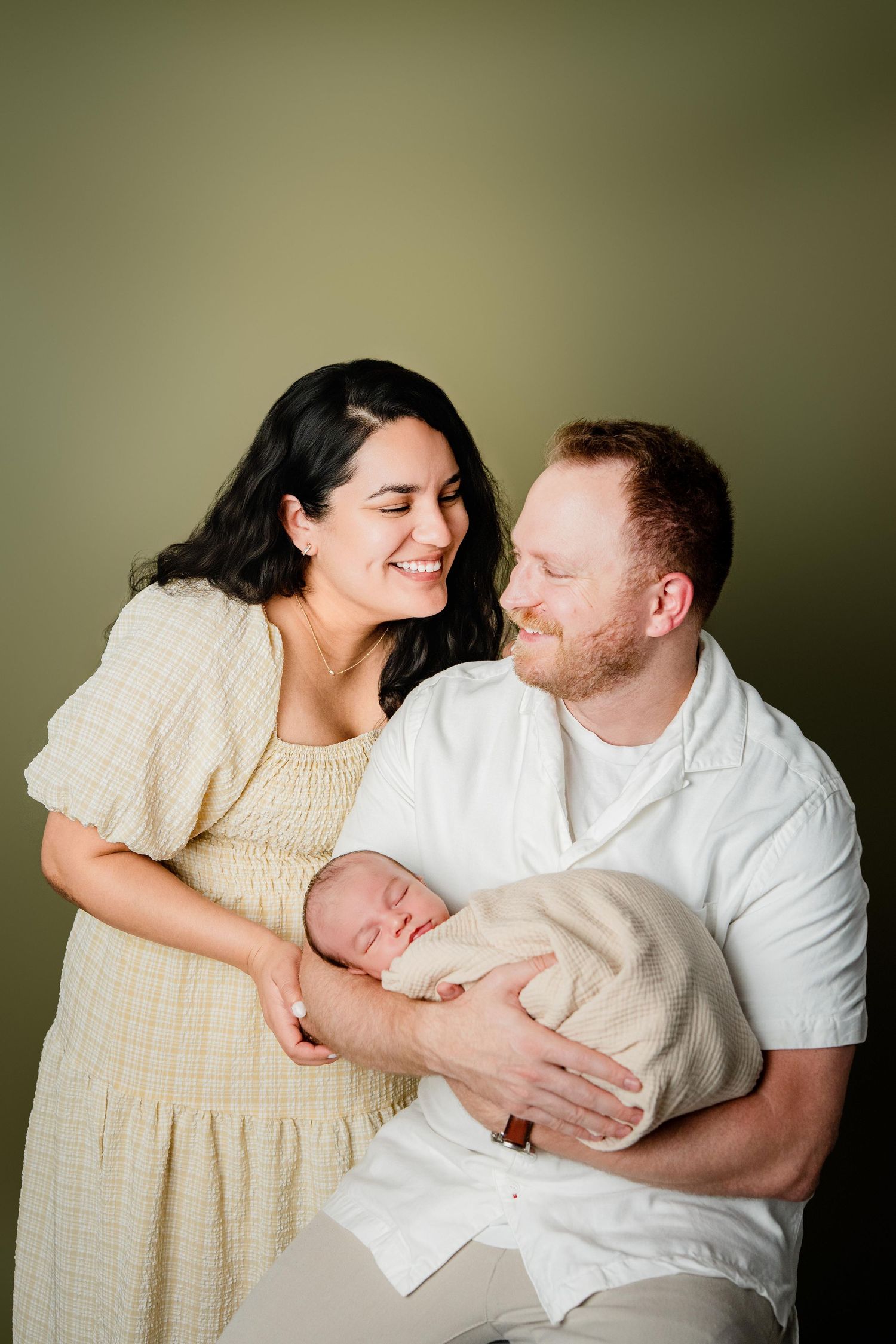 A couple shares tender moments while sitting together in a soft neutral setting with warm lighting.