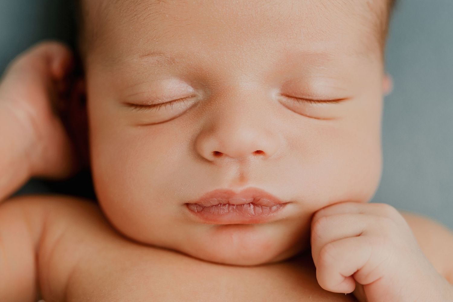 Closeup series of a sleeping newborn baby's peaceful facial features against a soft blue background.
