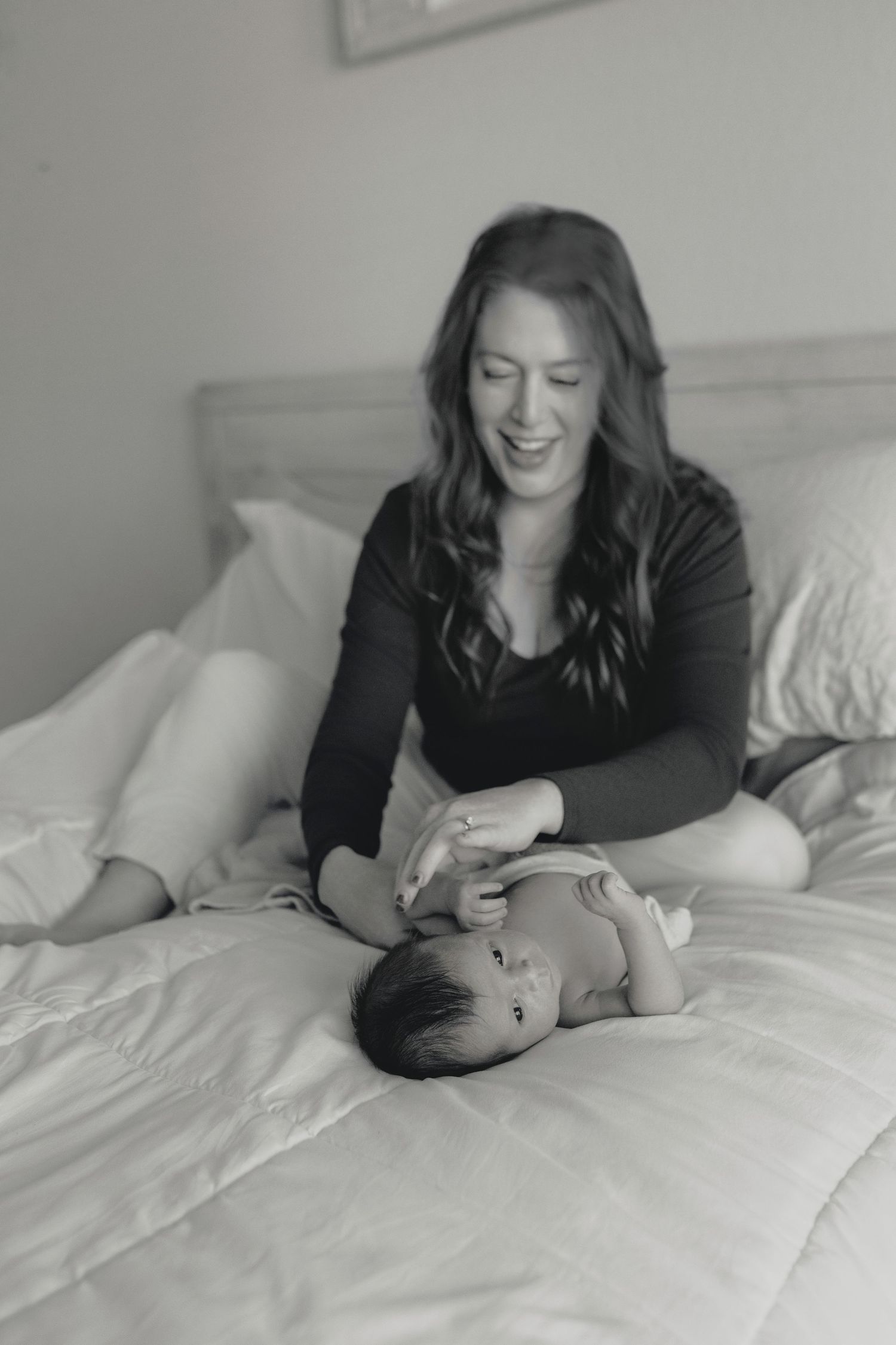 A tender black and white photo series showing a mother and baby sharing intimate moments on a white bed.
