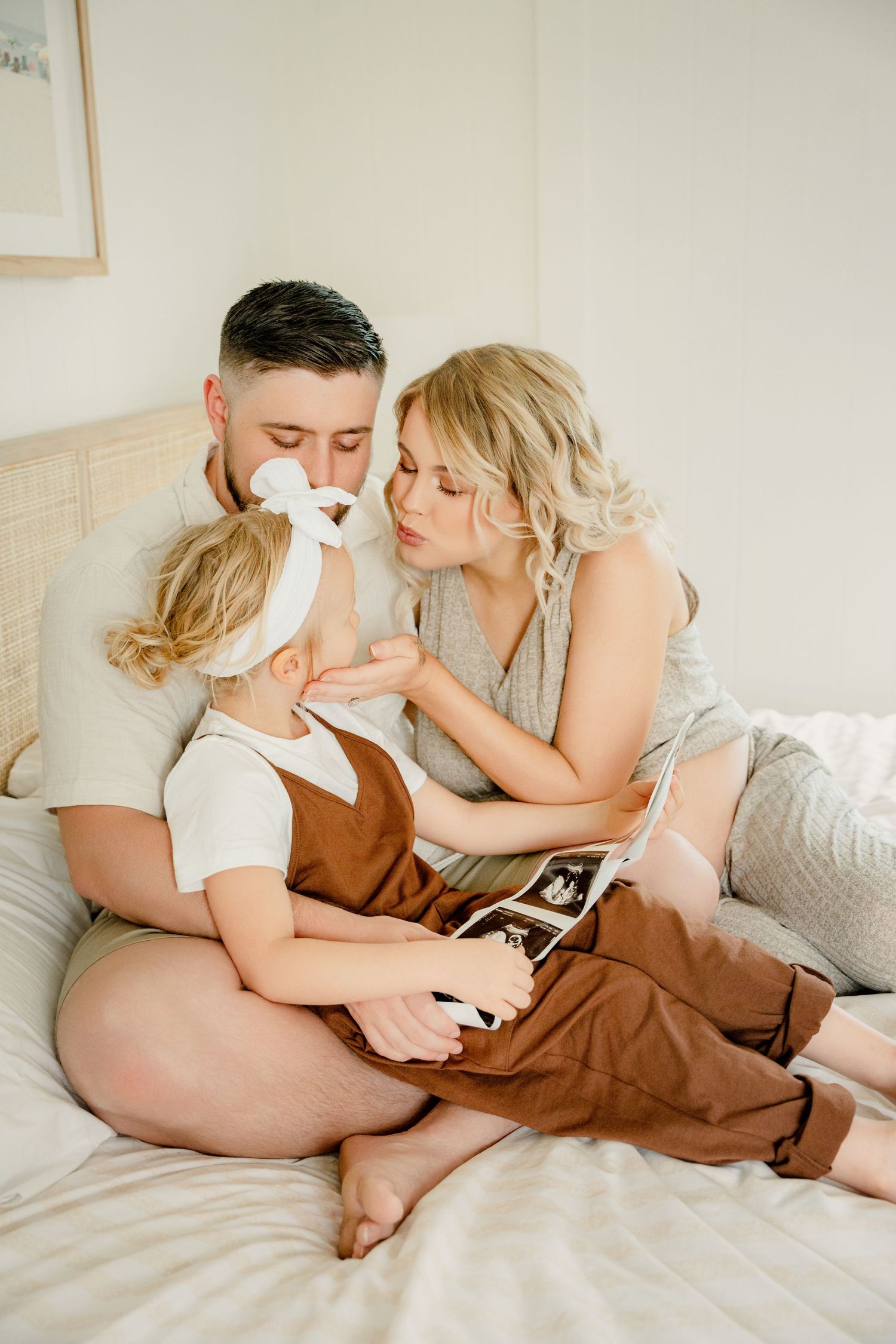 A family shares an intimate moment together on a bed while looking at ultrasound photos.