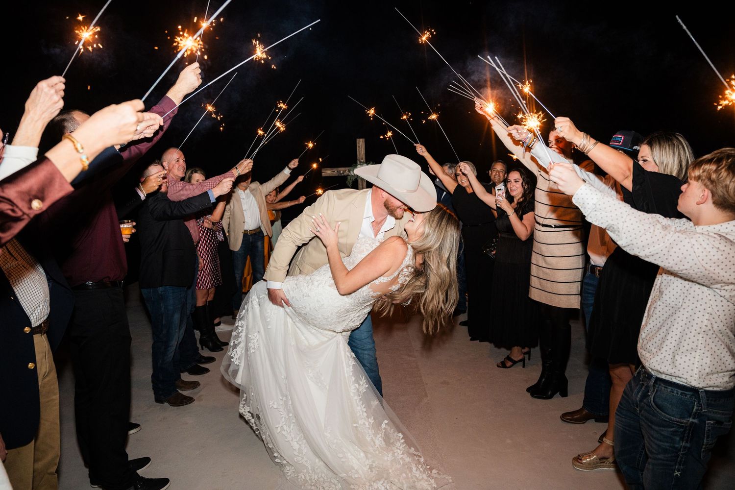 Wedding sparkler exit with couple sharing romantic dip kiss under glowing lights.