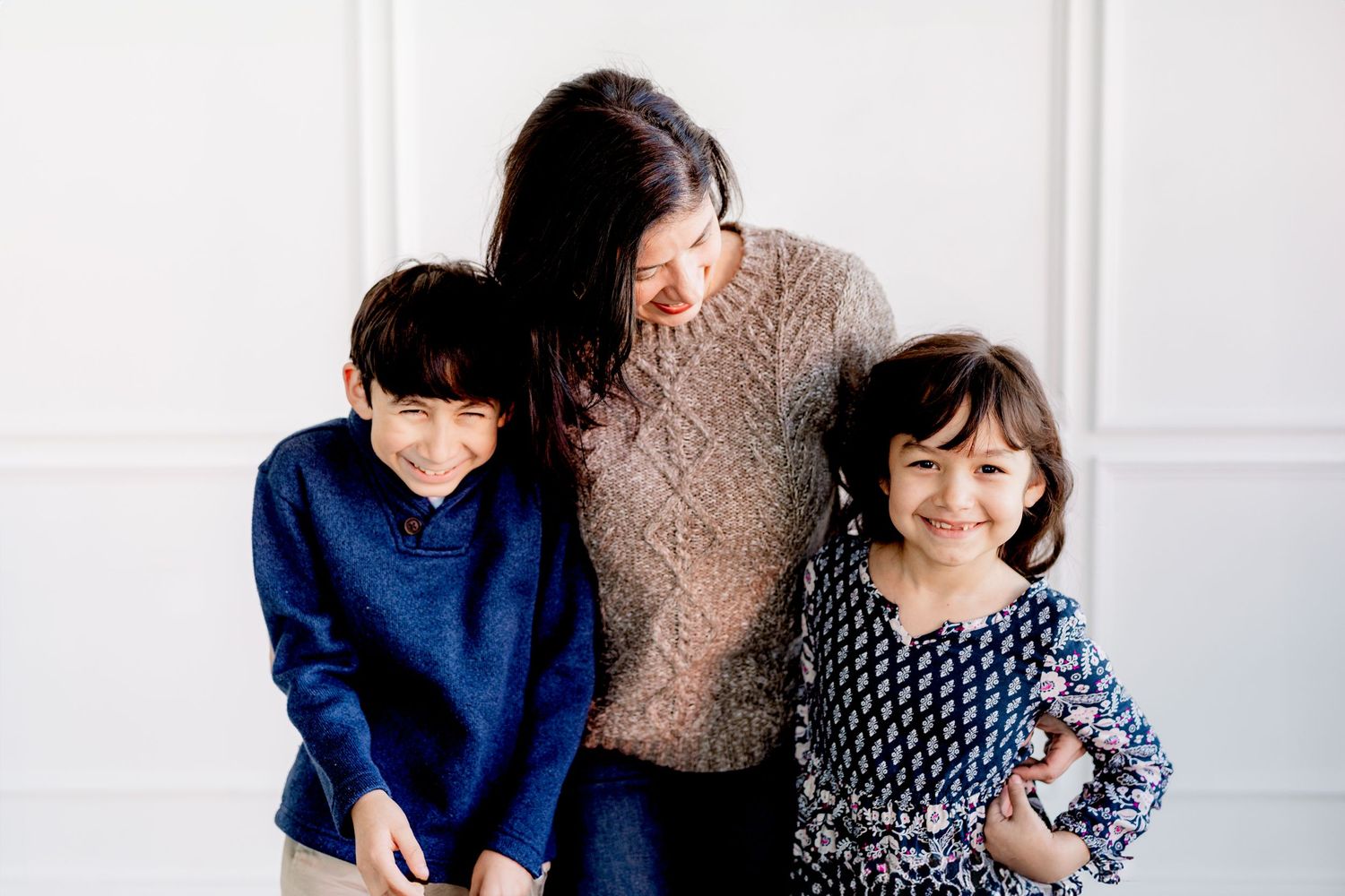 Three people pose together against a white wall wearing casual winter outfits.