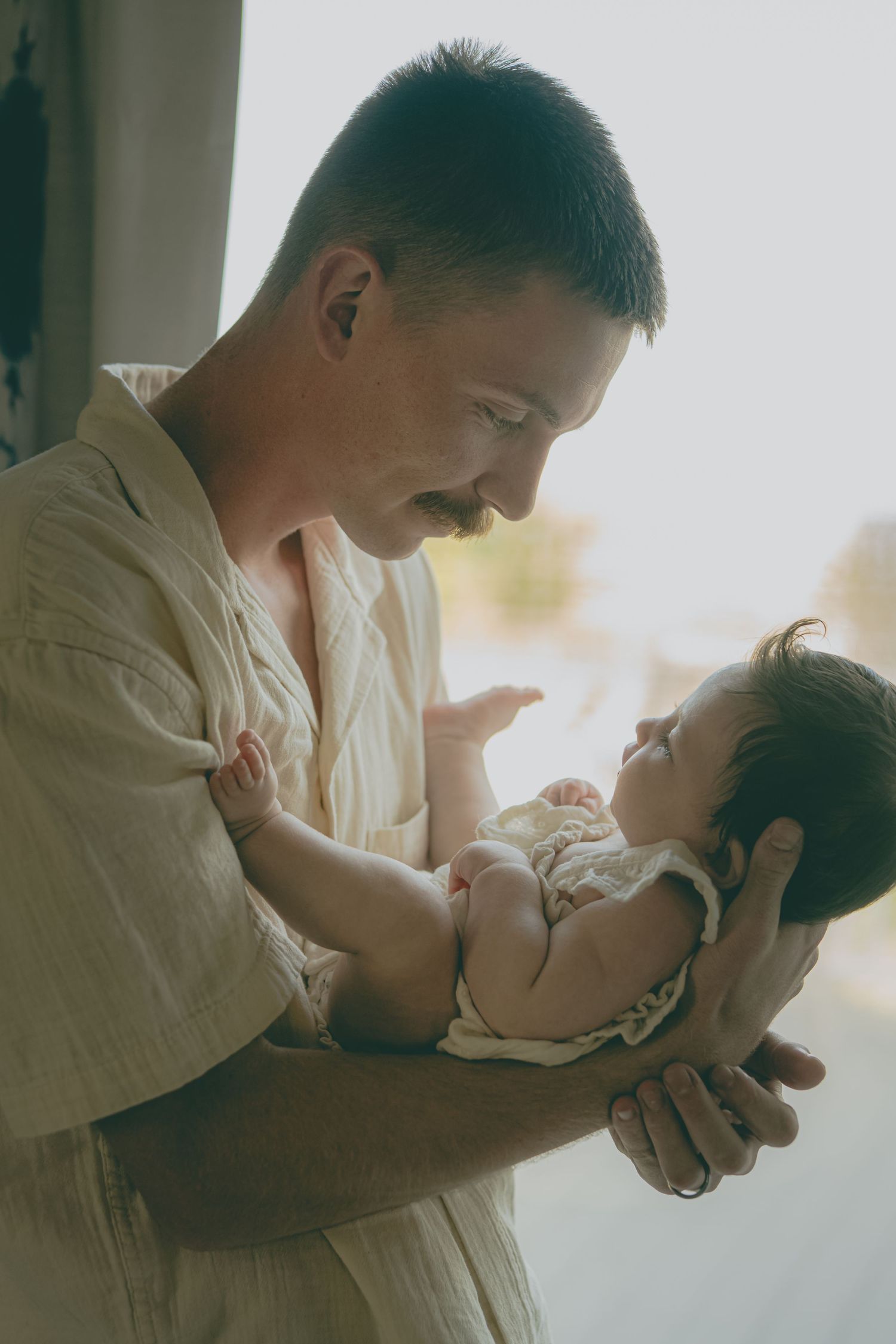 A tender moment between parent and baby in soft natural lighting, creating an intimate portrait of early parenthood.