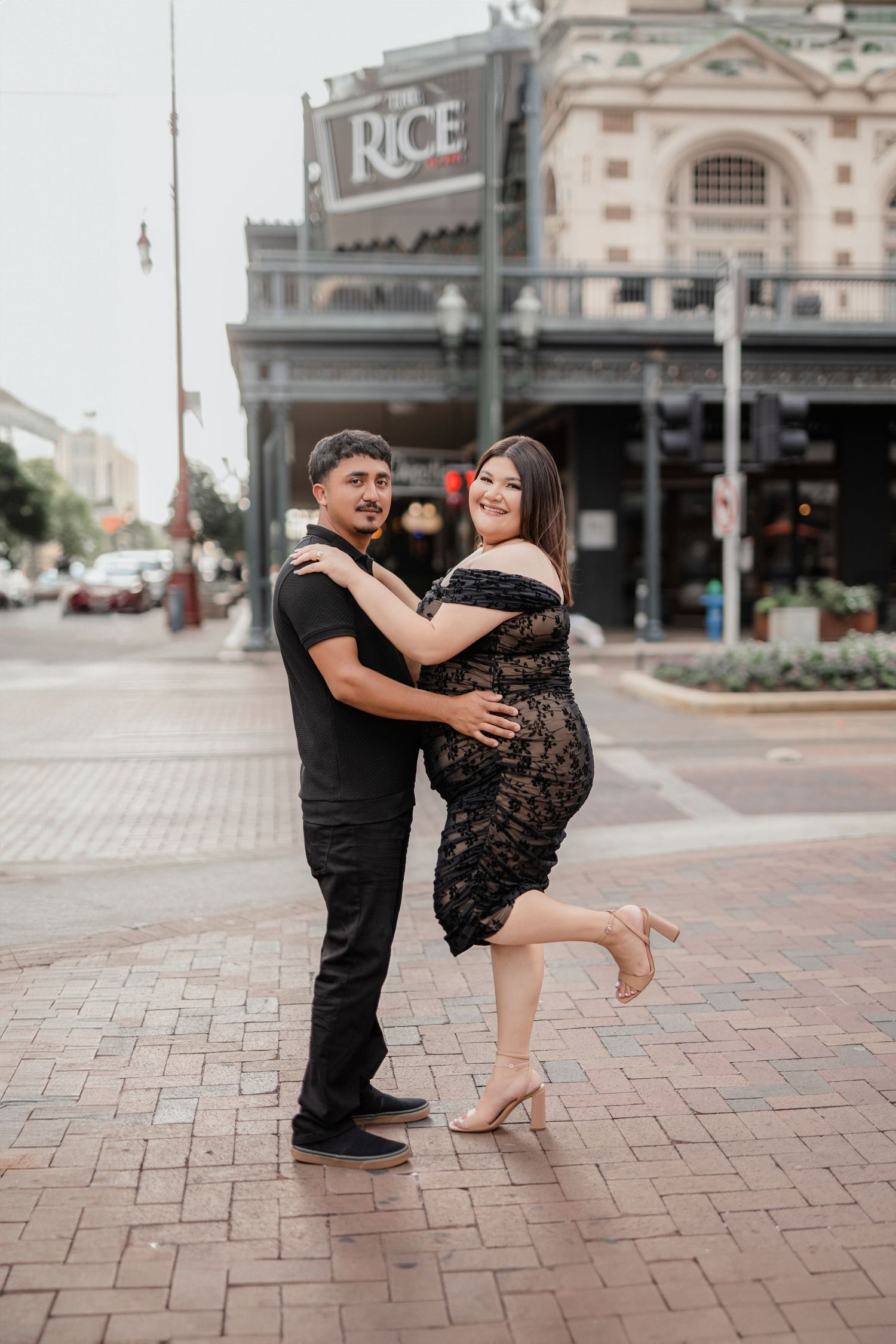 Couple performs romantic dance moves on brick pavement outside historic Rice building in downtown setting.