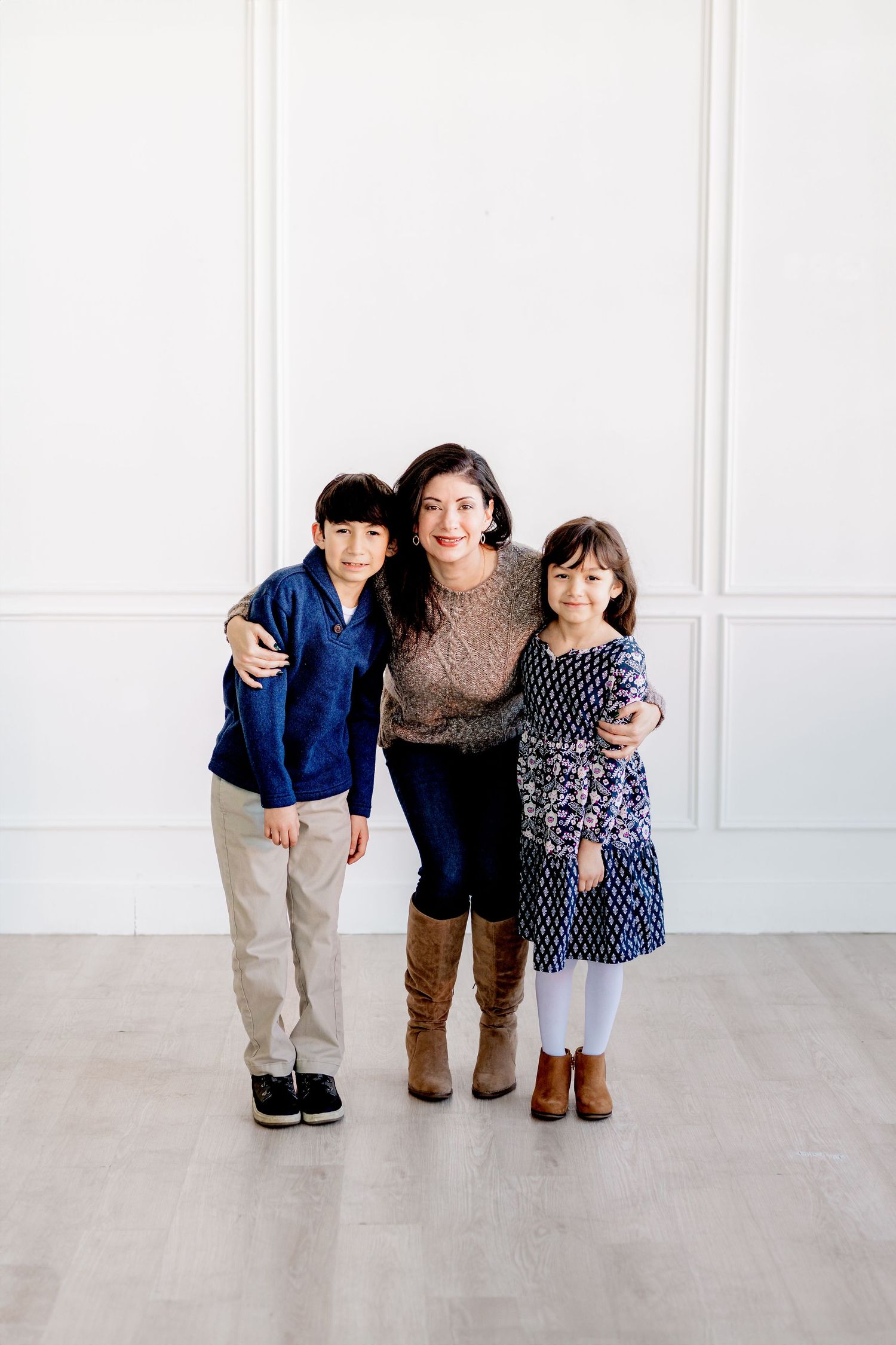 Three people pose together against white paneled wall in coordinated casual outfits.