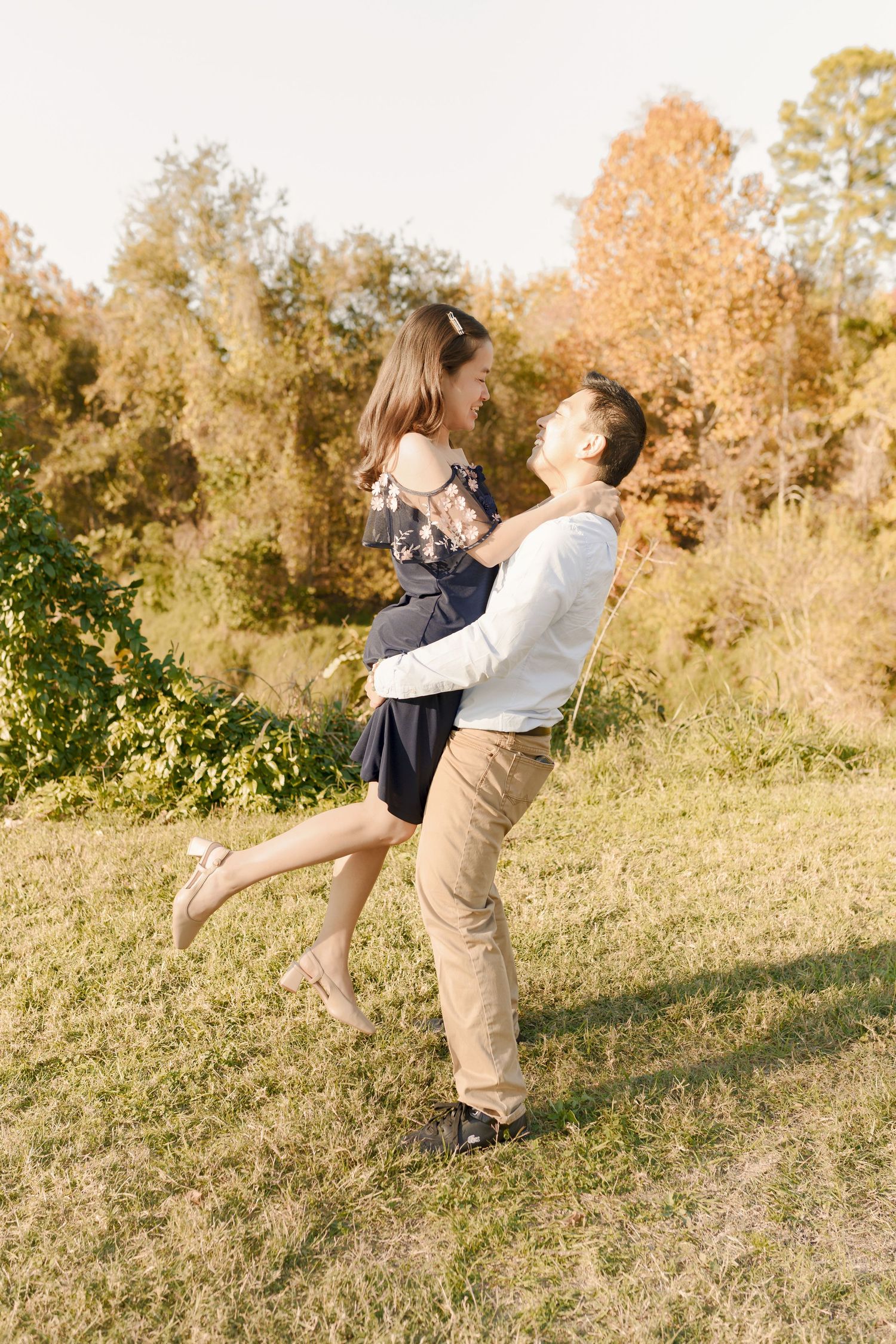 A couple embraces and spins together on a grassy hillside during golden hour with autumn foliage in the background.