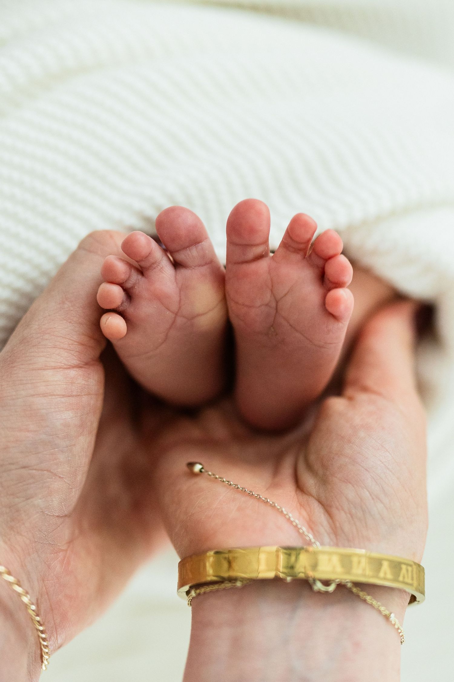 Tiny newborn feet resting in adult hands wearing gold bracelet.