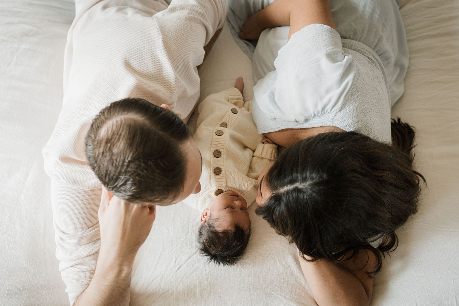 A series of black and white photos showing a couple lying together in intimate poses on white bedding.