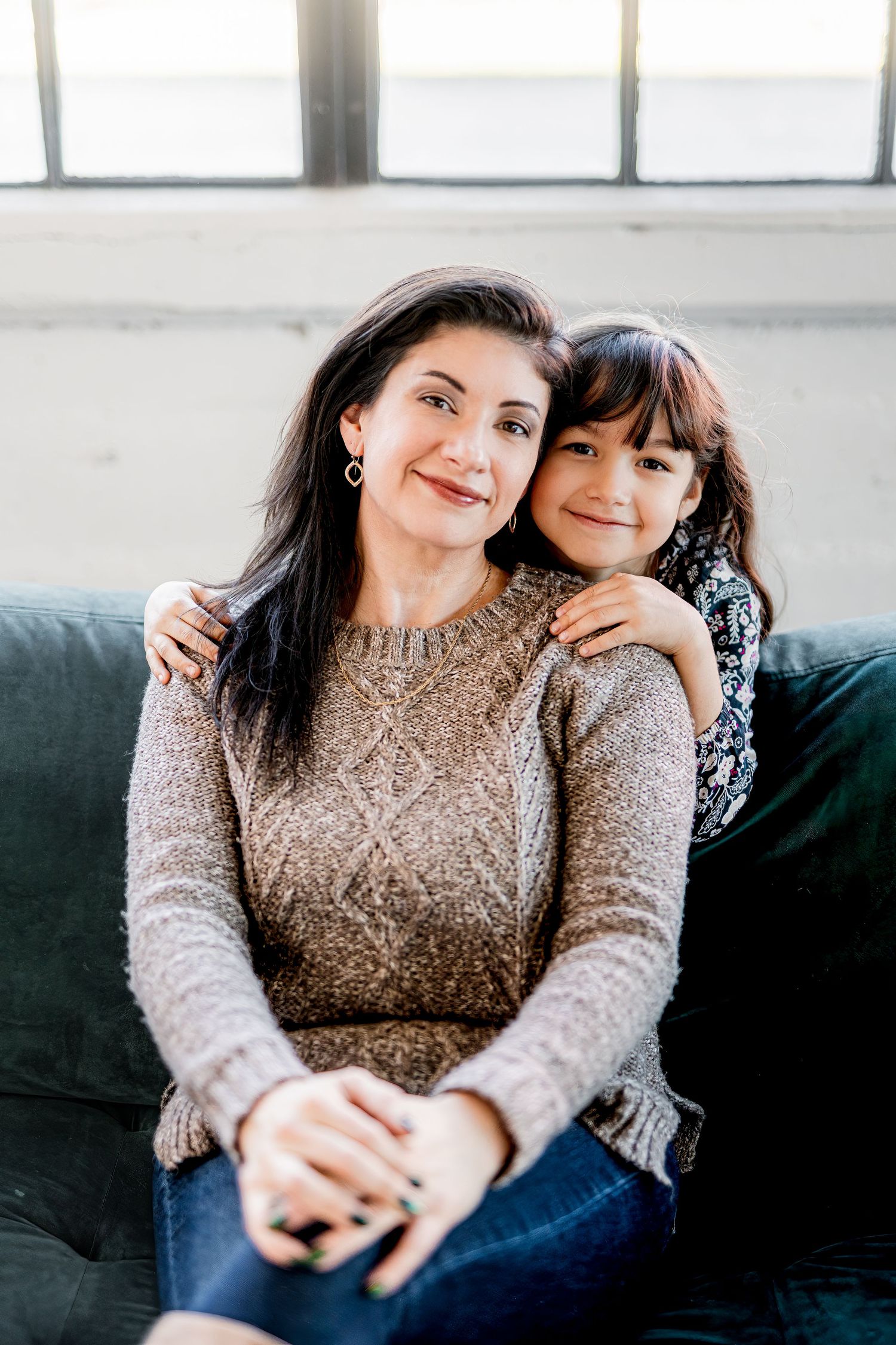 Cozy portrait of two people wearing matching sweaters sitting together on blue couch.