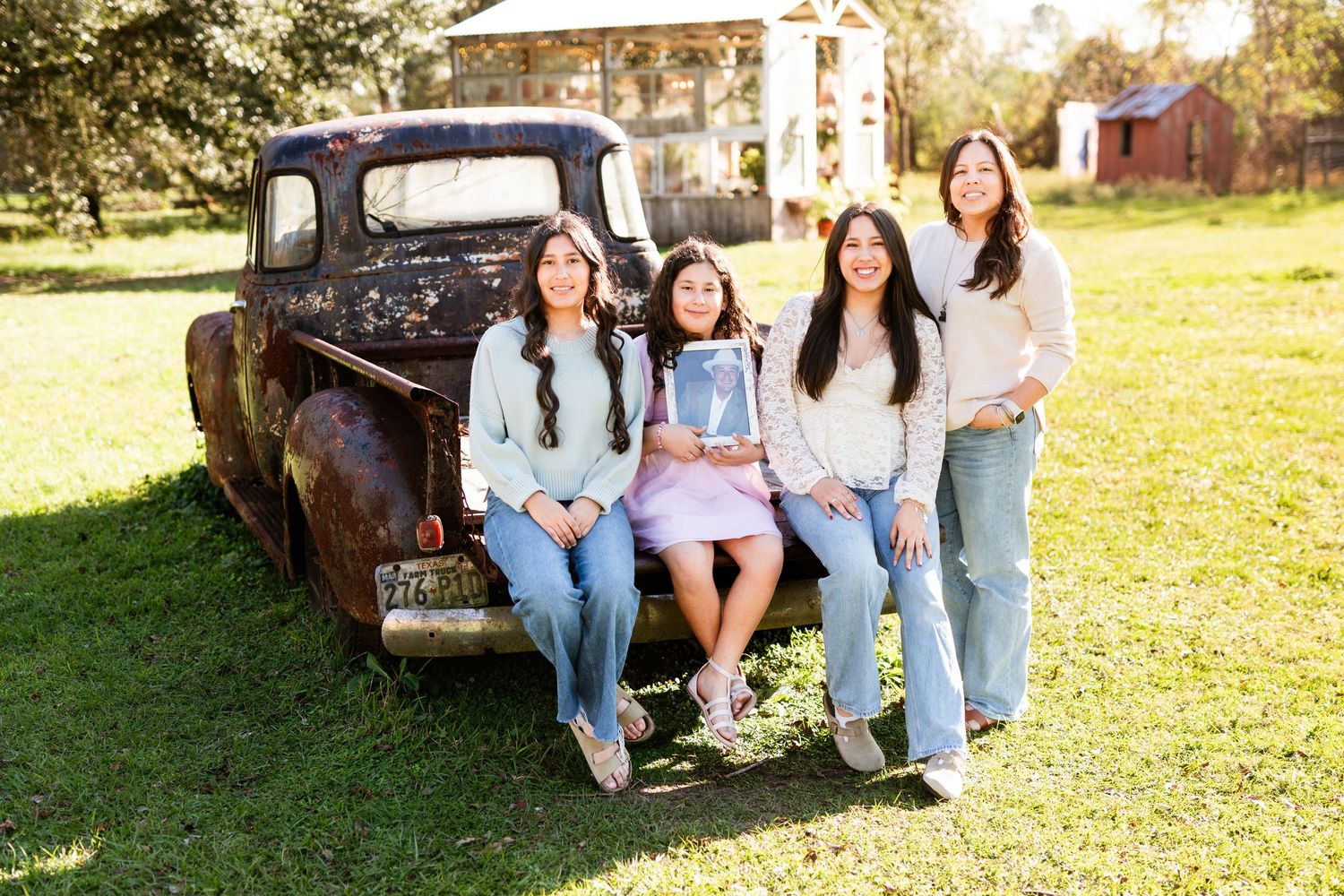 Group posing casually on vintage black pickup truck in rustic outdoor setting.