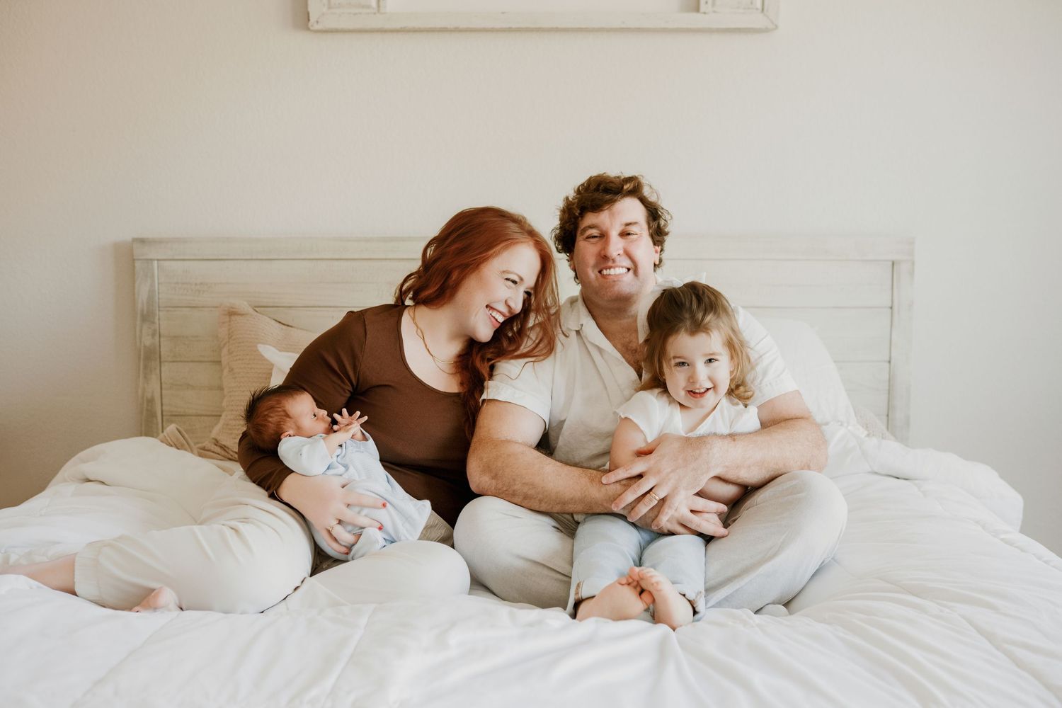 Family members lying together on white bedding while sharing tender moments of connection and affection.