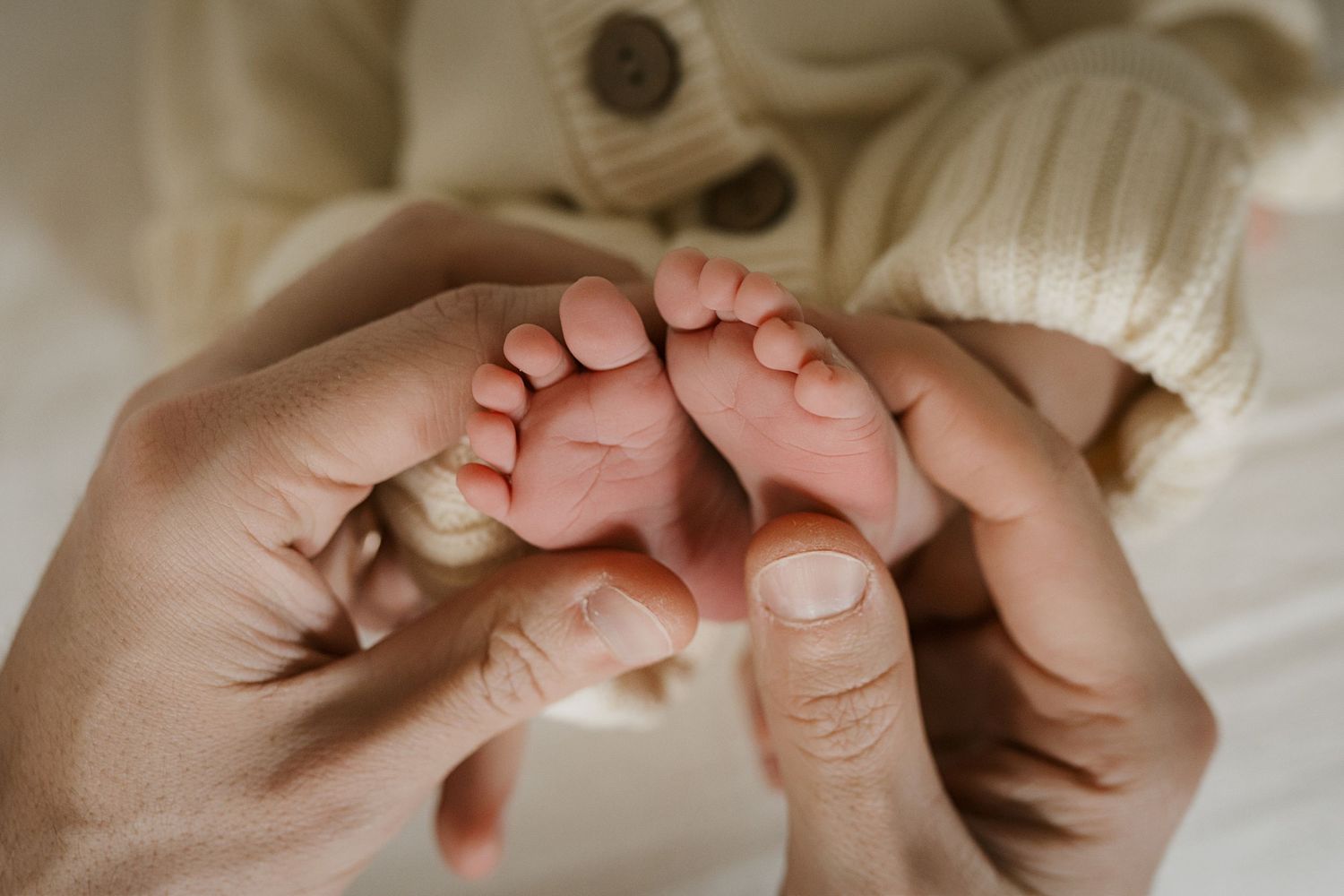 Close-up view of tiny newborn baby feet being gently held by adult hands against white bedding.