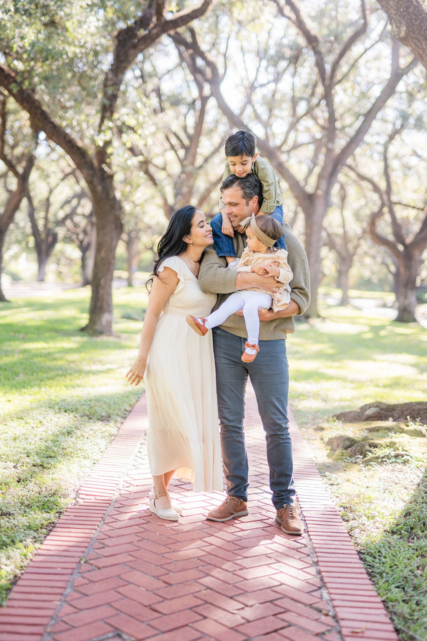 A loving family moment captured on a brick pathway surrounded by trees in a park.