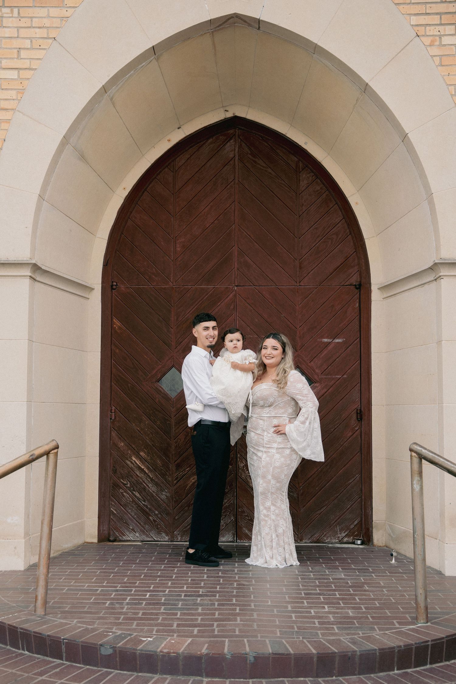 A couple poses in formal attire under an arched church doorway.