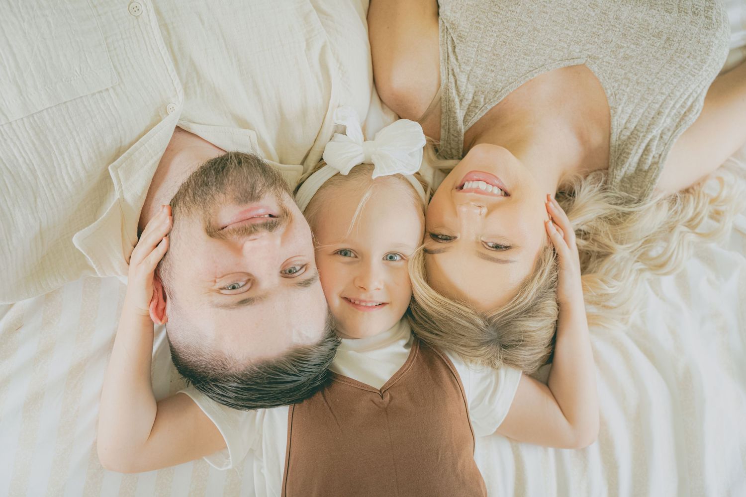 Three people lying together on white bedding in a circle formation, photographed from above.