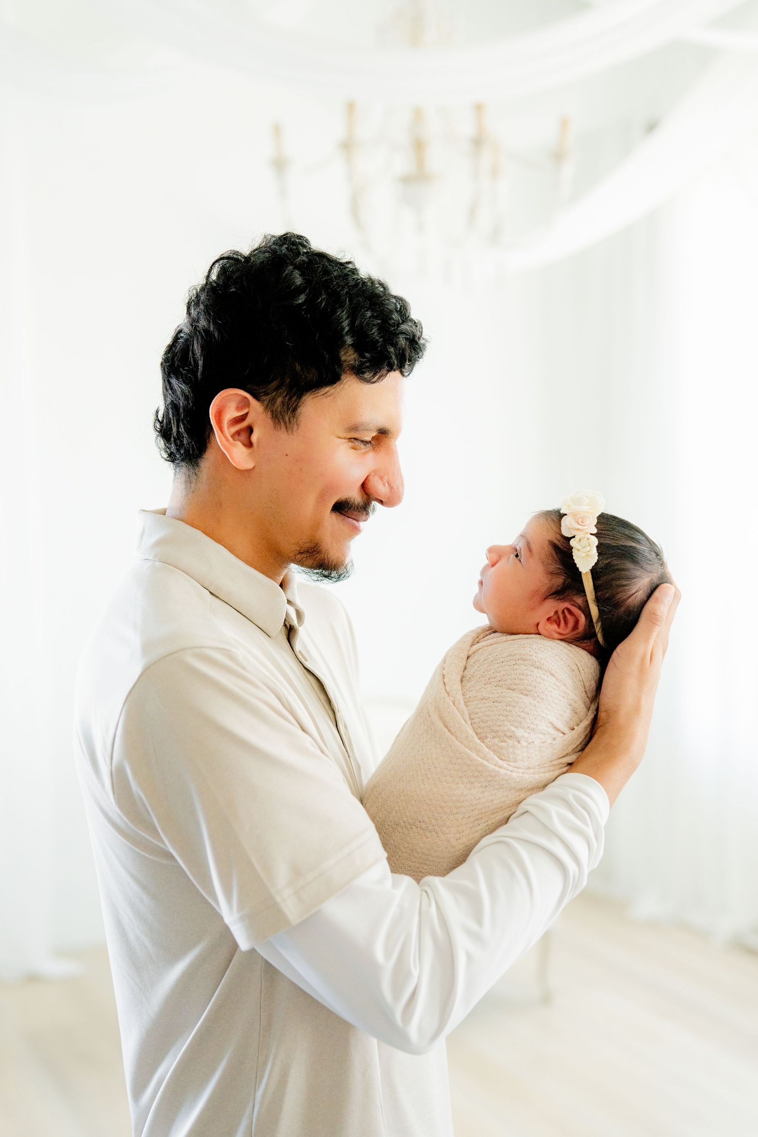 A tender moment between a parent and newborn baby in soft lighting against a white background.