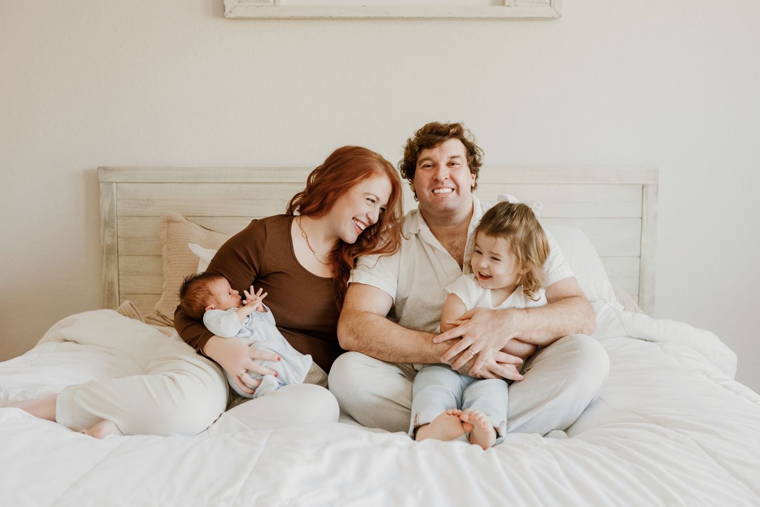 A tender moment between a couple and child snuggling together on a white bed in matching casual attire.