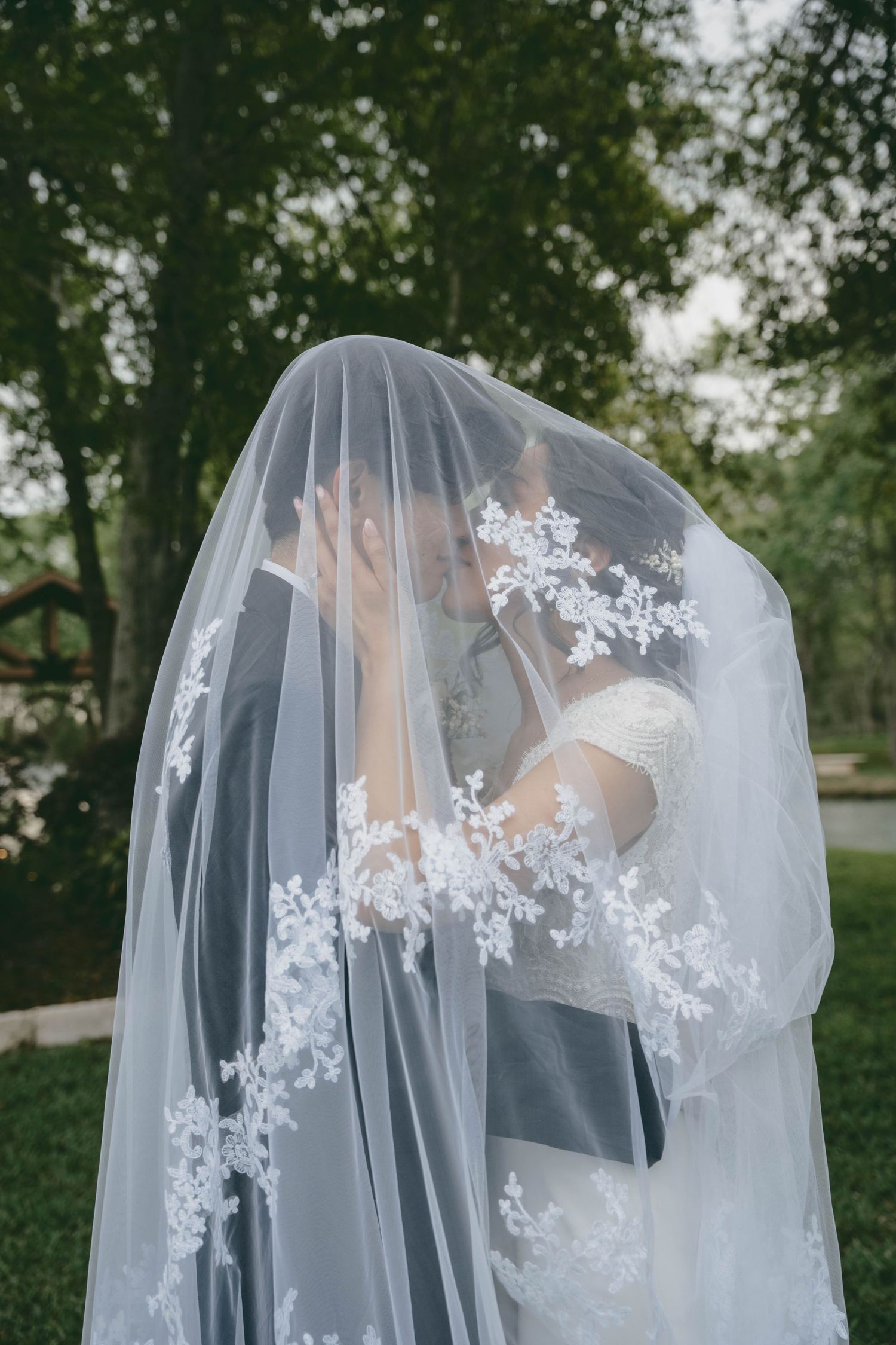 A romantic wedding moment captured through a delicate white lace veil in a garden setting.