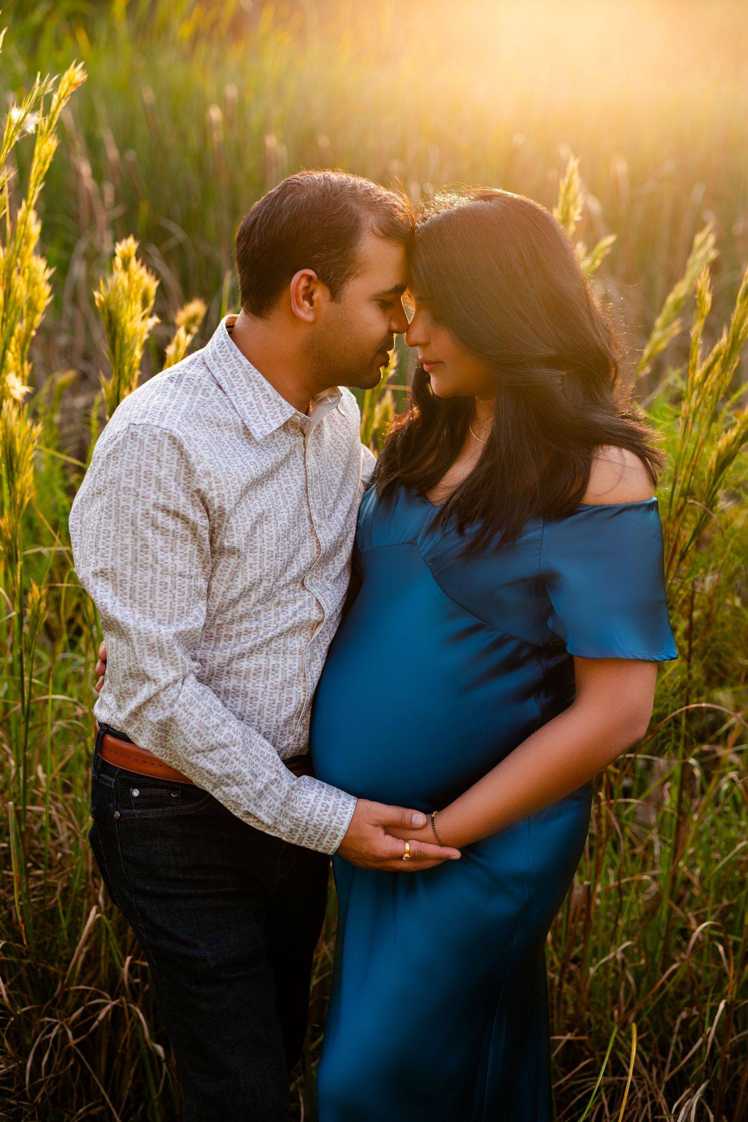 Romantic sunset maternity photo of couple embracing in tall golden grass.