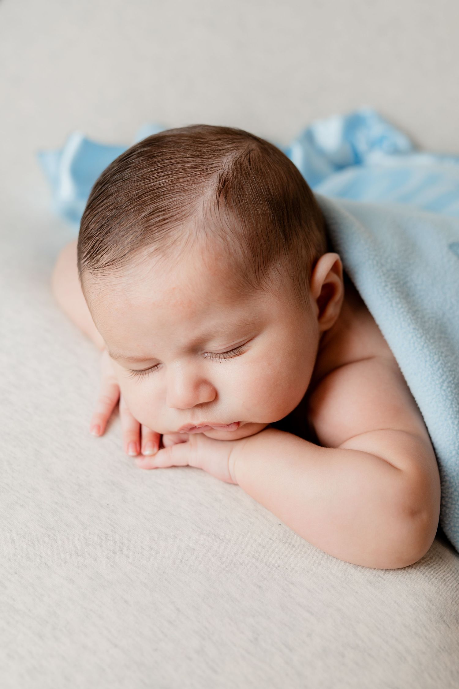 A peaceful sleeping baby wrapped in light blue blanket rests on soft white fabric during a newborn photoshoot.