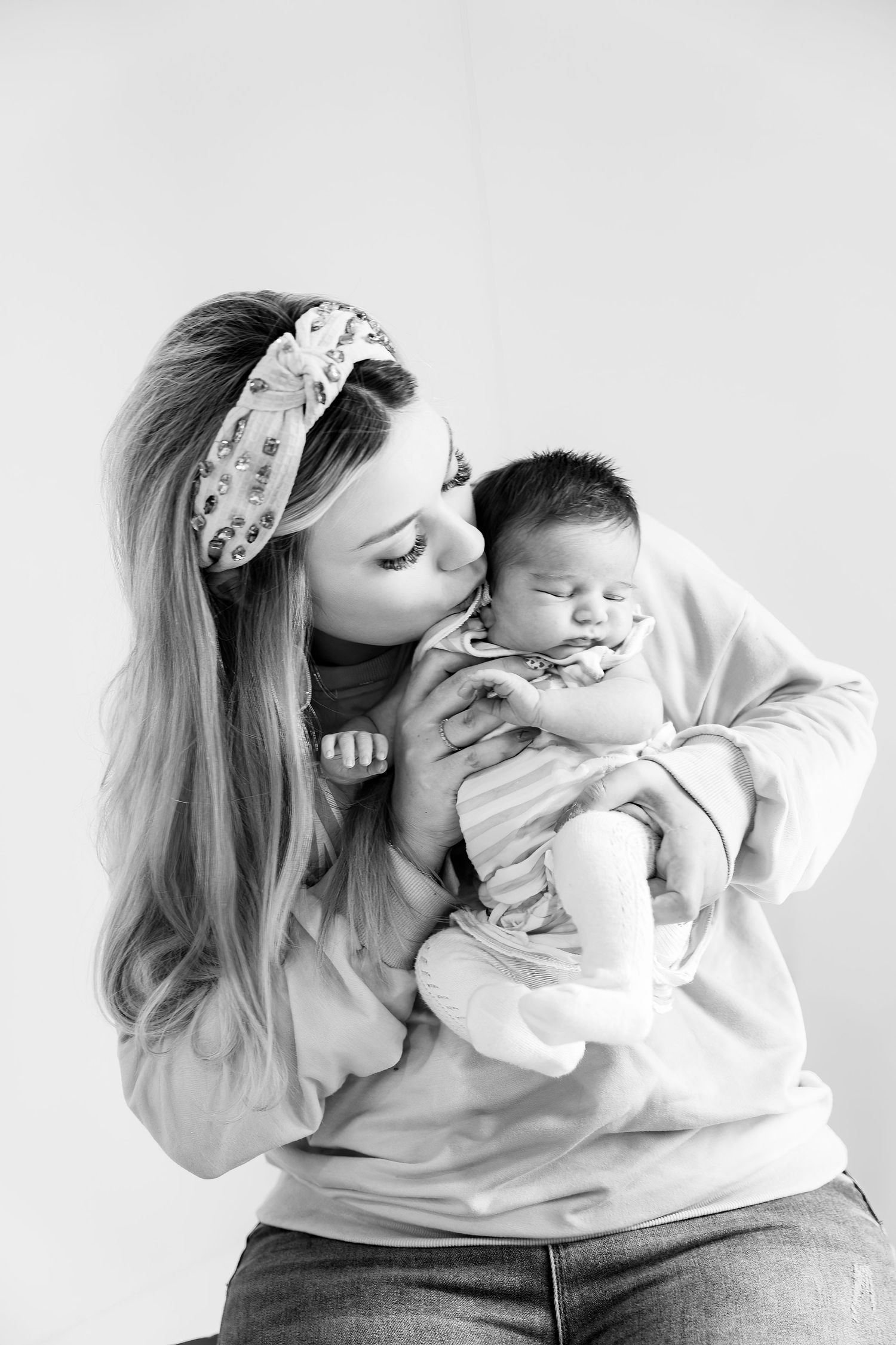 A tender black and white portrait of parent kissing baby while wearing a floral headband.