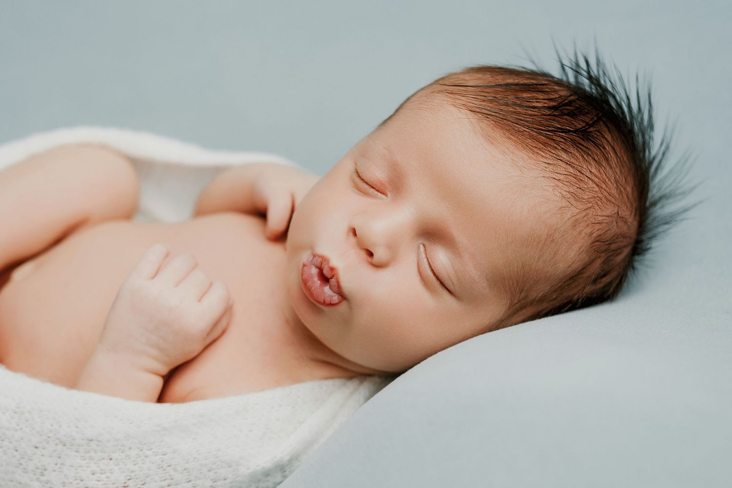 A sleeping newborn baby lies peacefully on soft white fabric in a series of connected photos.