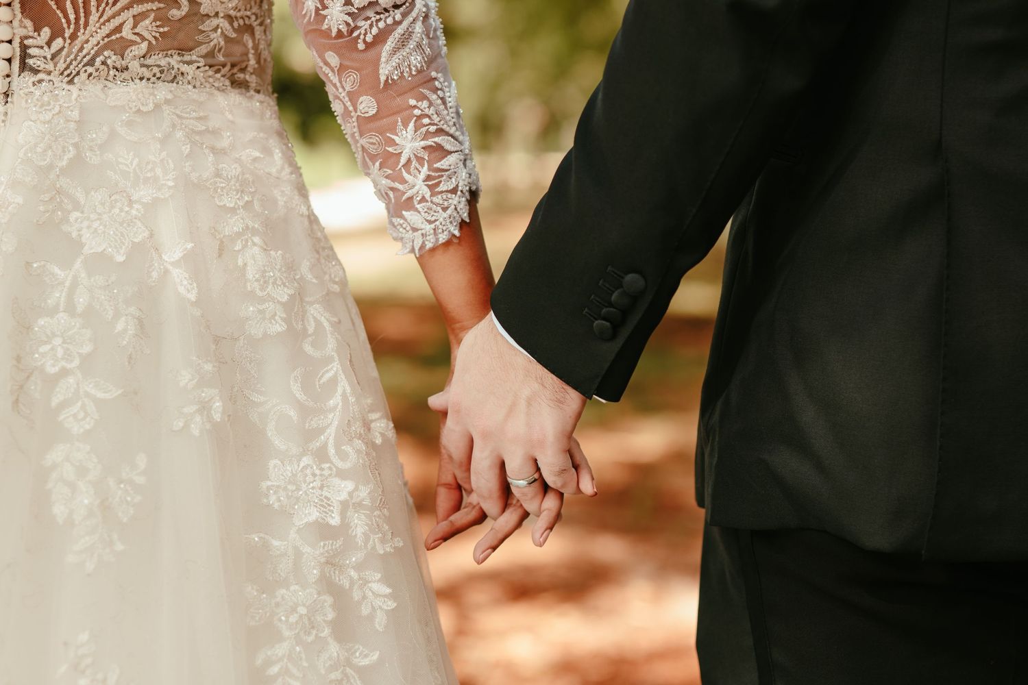 Close-up detail of a bride and groom holding hands showing lace sleeve details.
