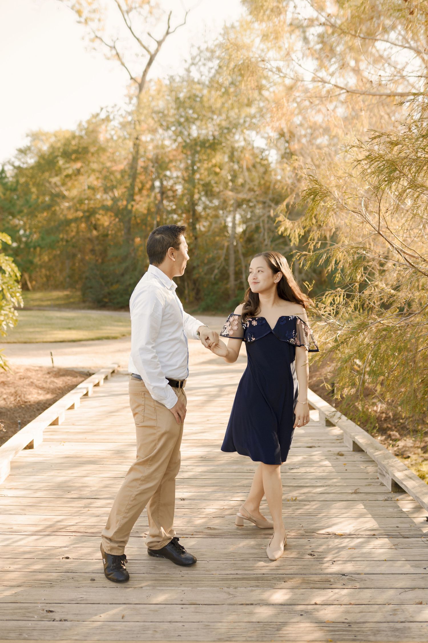 A couple shares a romantic moment dancing together on a wooden boardwalk surrounded by autumn trees.