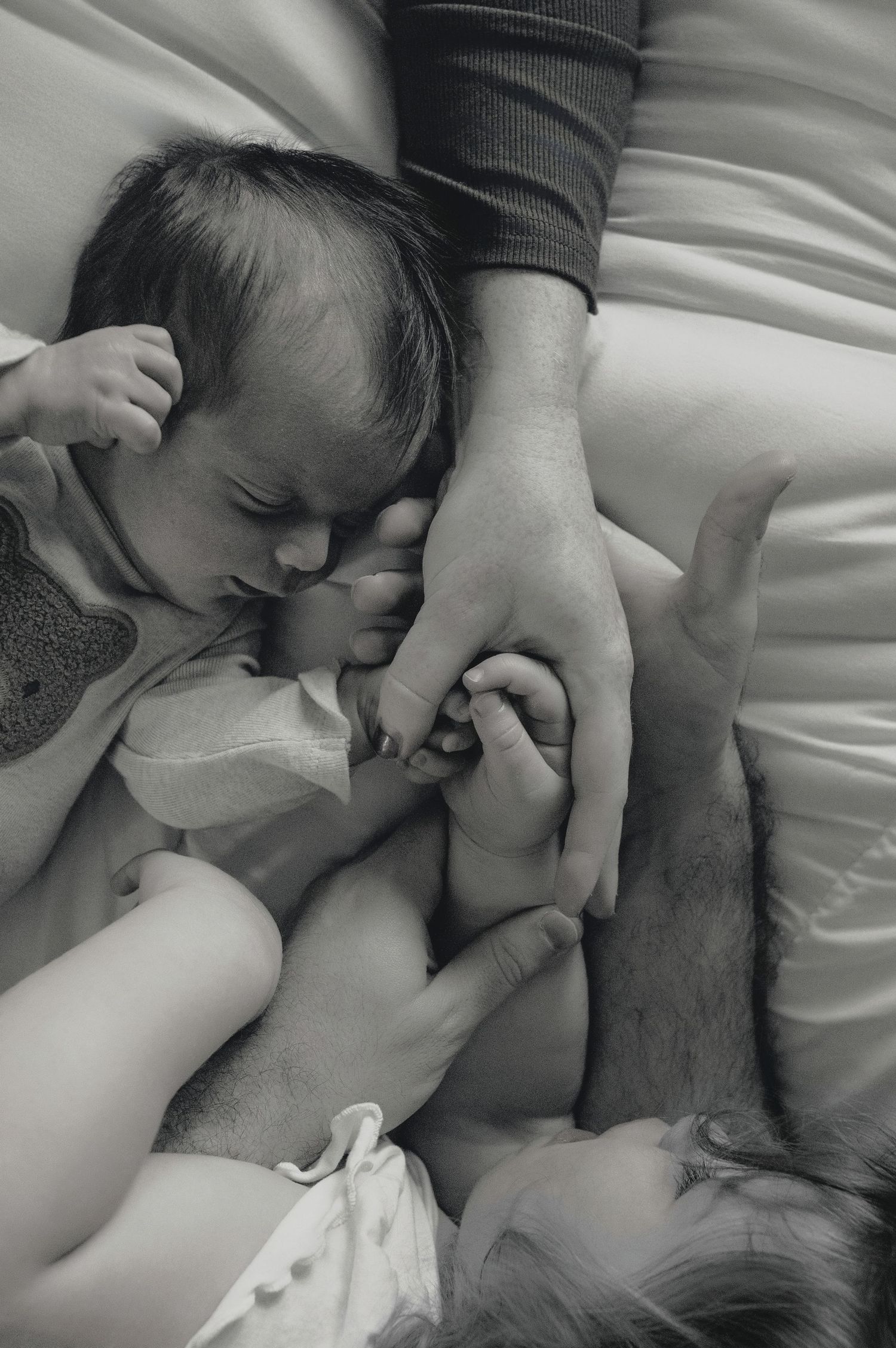 A series of black and white photographs showing intimate romantic moments between two people lying on white bedding.