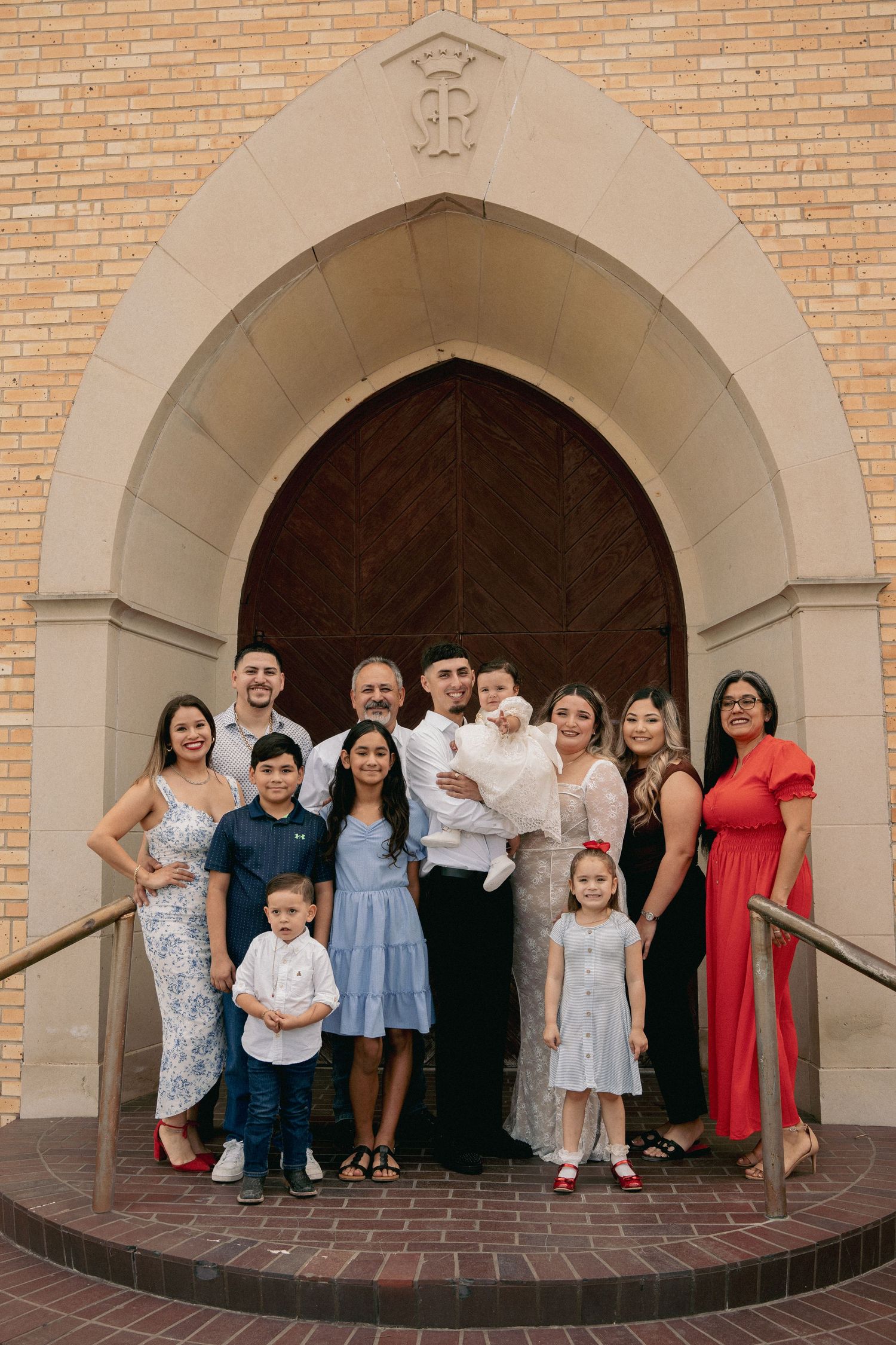 A group of people standing together on brick steps in front of a large arched church doorway.