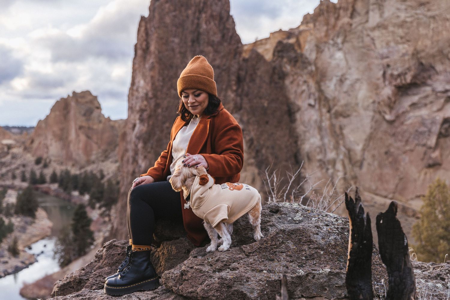 Female presenting person and a small dog, sitting on a rock, overlooking Smith Rock in Oregon.