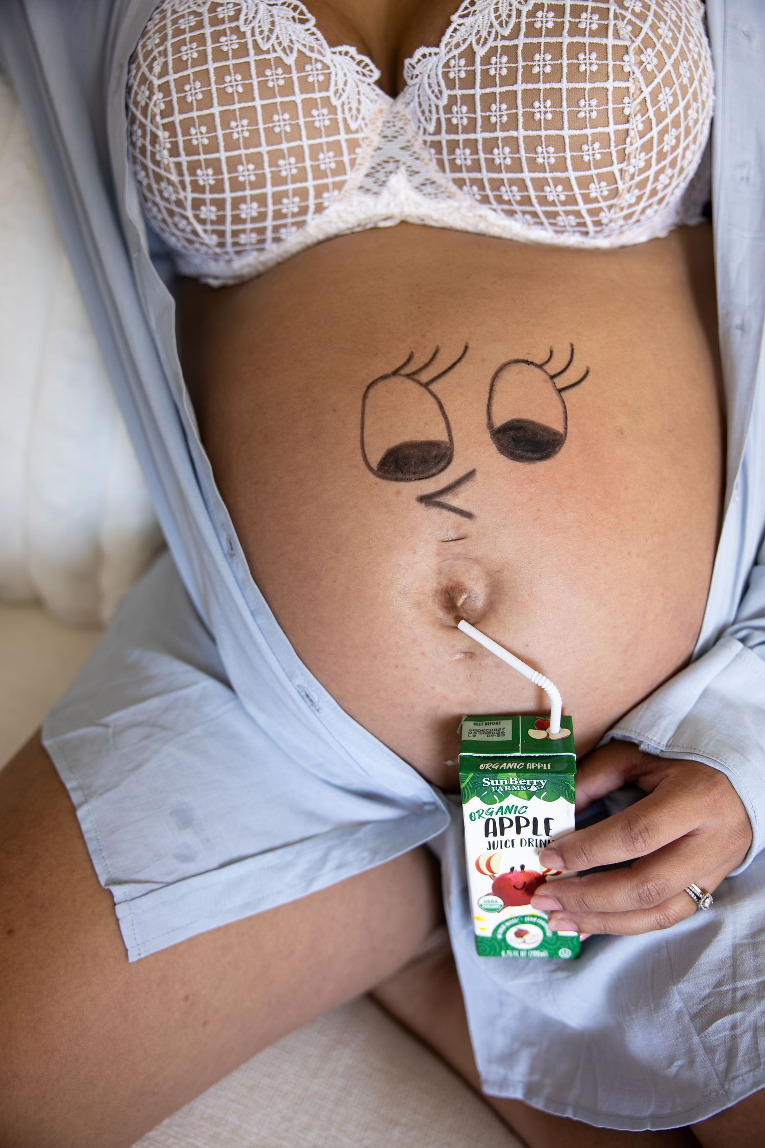 Pregnant woman with a cute face drawn on her baby bump holding an apple juice carton with a straw.