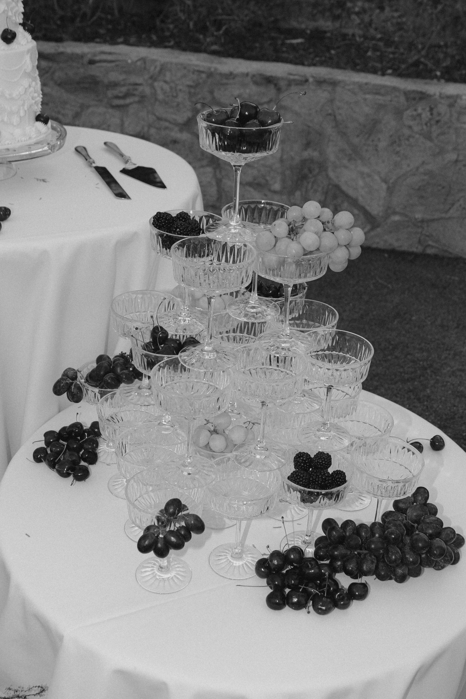 Elegant tower of champagne glasses with scattered grapes on a white tablecloth at a wedding reception.
