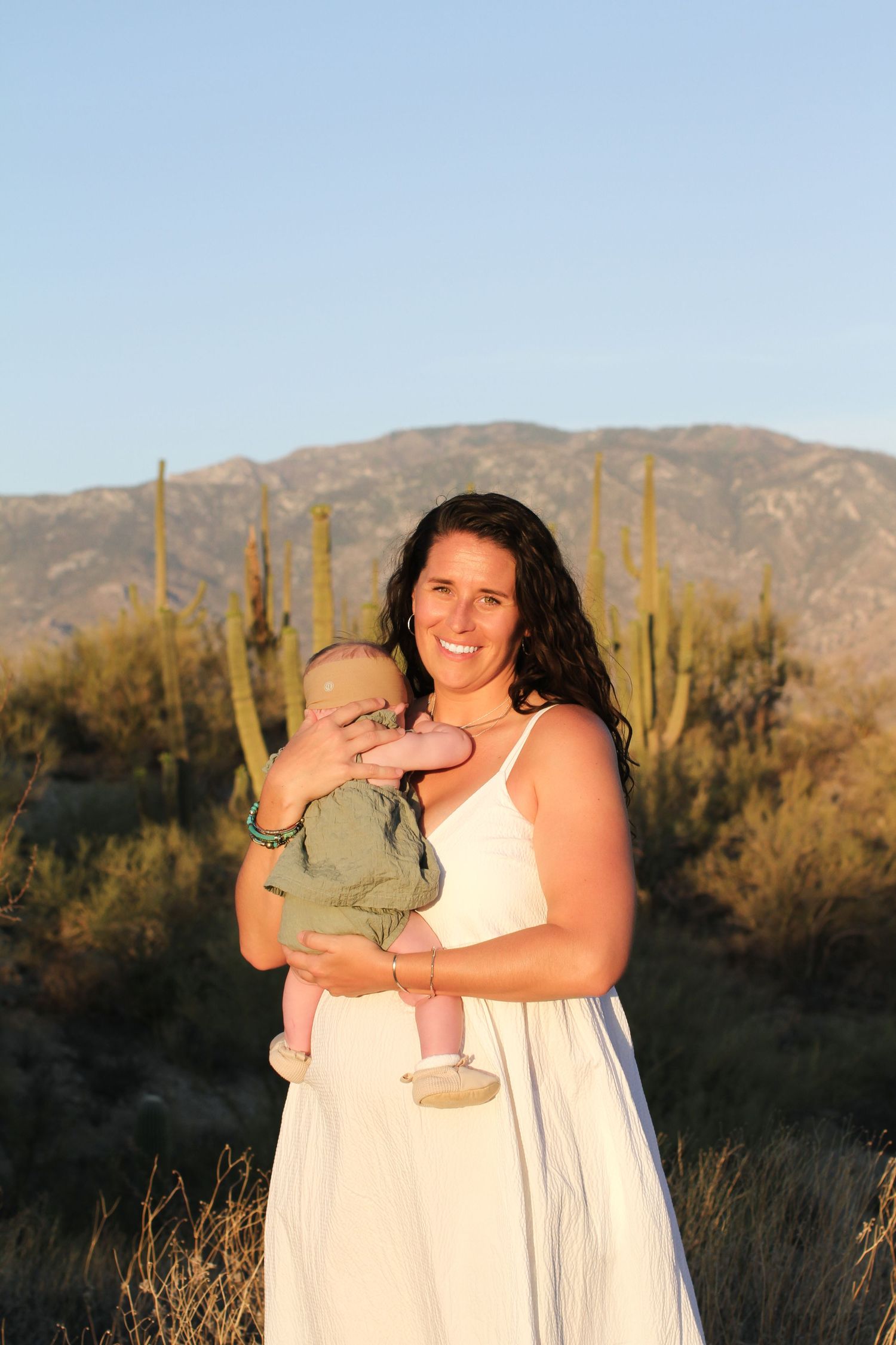 A desert photoshoot features a couple in white clothing with saguaro cacti in the background.