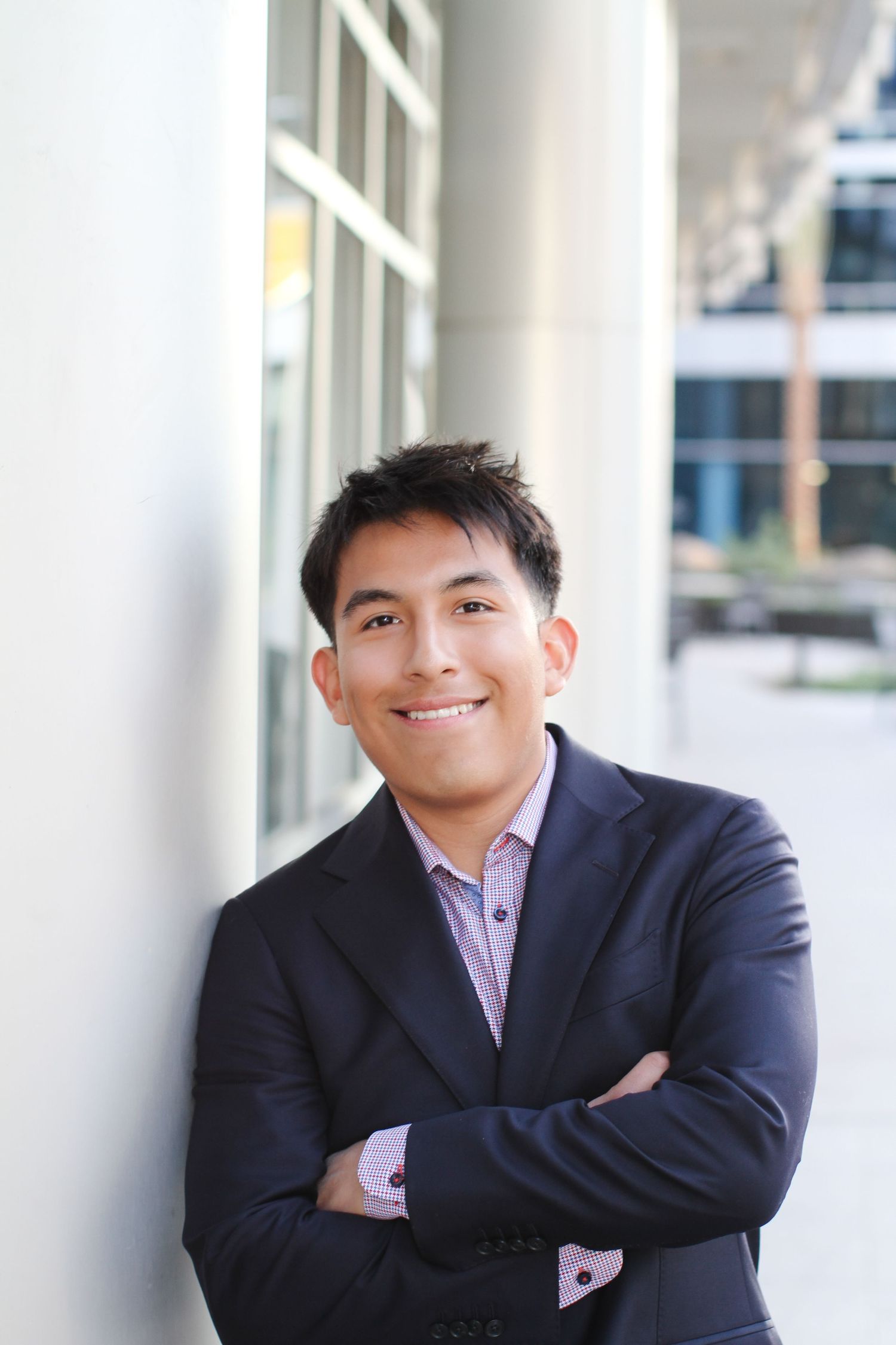 Professional portrait of person in business suit leaning against white column with crossed arms.